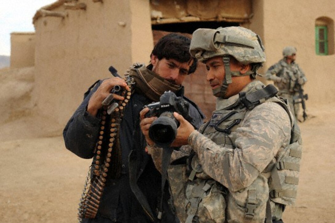 U.S. Air Force Tech. Sgt. Efren Lopez, 4th Combat Camera Squadron, shows digital photographs to an Afghan soldier in Shabila Kalan, Zabul province, Afghanistan. (courtesy photo)