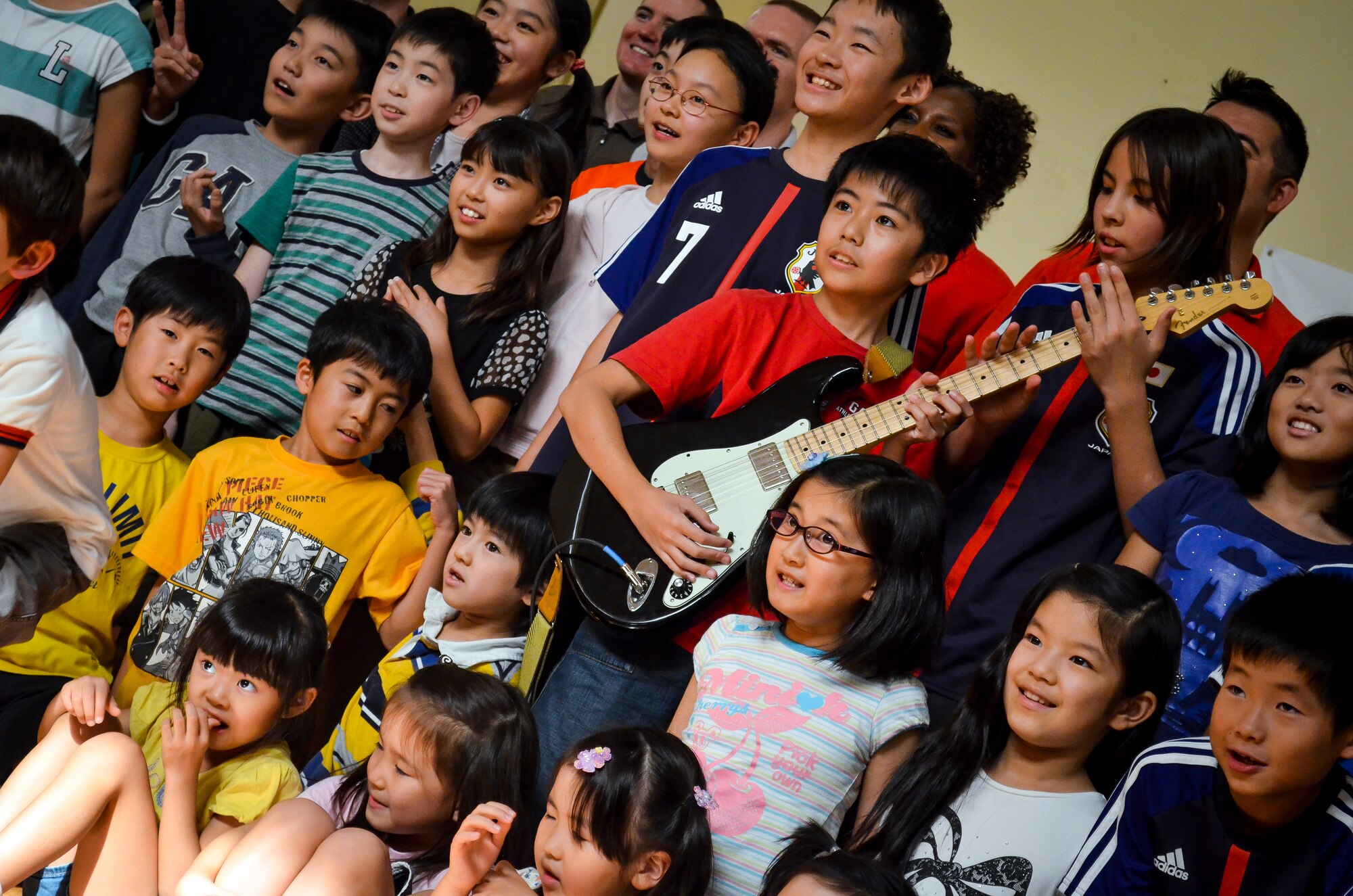 Children attending the Japan School of Doha pose for a group photo with a guitar after a performance by the Air Forces Central Command’s band, “Hypersonic,” in Doha, Qatar, April 23, 2014. The band’s mission, which is to promote troop morale, diplomacy and outreach to host nation communities, touched home when playing for the Japanese, as the band is deployed from Yokota Air Base, Japan. (U.S. Air Force photo/Senior Airman Jared Trimarchi) 
