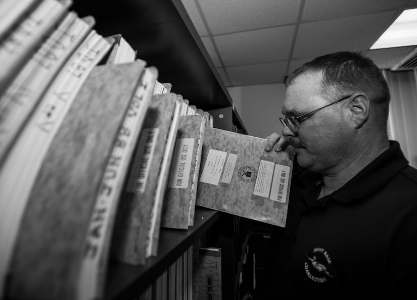 Stan Gohl, 437th Airlift Wing historian, removes a paper copy of an older 437 AW history; today completed histories are maintained digitally on CDs and DVDs April 22, 2014. Most history offices also maintain a repository of photos, videos, and other multimedia capturing the history of the base and its assigned units.  (U.S. Air Force photo/ Senior Airman Dennis Sloan)