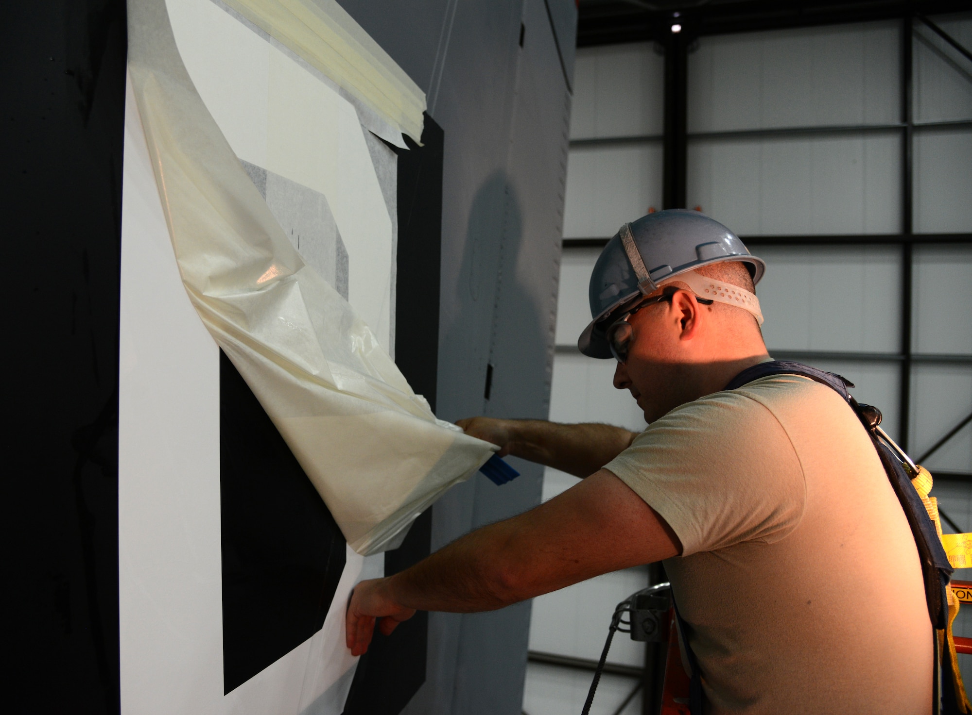 U.S. Air Force Tech. Sgt. Timothy Farmakis, 100th Maintenance Squadron NCO in charge of corrosion control from Las Vegas, peels off the cover sheet on a new “Square D” tail flash April 24, 2014, in Hangar 814 on RAF Mildenhall, England. All writing on the aircraft is hand-painted aside from the nose art, tail flash and the markings on the boom. (U.S. Air Force photo by Airman 1st Class Kelsey Waters/Released)