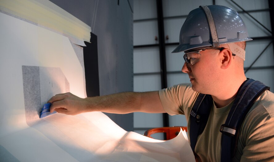 U.S. Air Force Tech. Sgt. Timothy Farmakis, 100th Maintenance Squadron NCO in charge of corrosion control from Las Vegas, smoothes a white “D” into a black painted square on the tail of a KC-135 Stratotanker April 24, 2014, in Hangar 814 on RAF Mildenhall, England. The old tail flashes are one giant decal; the newer ones are now a white “D” placed on top of a painted black square. The change to a smaller “D” decal saves time on decal installation and replacement. (U.S. Air Force photo by Airman 1st Class Kelsey Waters/Released)