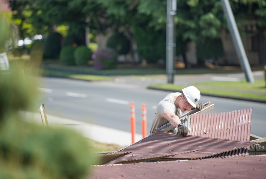 Senior Airman Kyle Smith, 374th Civil Engineer Squadron structures journeyman, removes a sheet of metal from a damaged roof at Yokota Air Base, Japan, April 24, 2014. Smith and three other Airmen worked together to remove the roof which posed a safety threat to dormitory residents ever since being damaged during heavy snow fall. (U.S. Air Force photo by Staff Sgt. Cody H. Ramirez/Released)