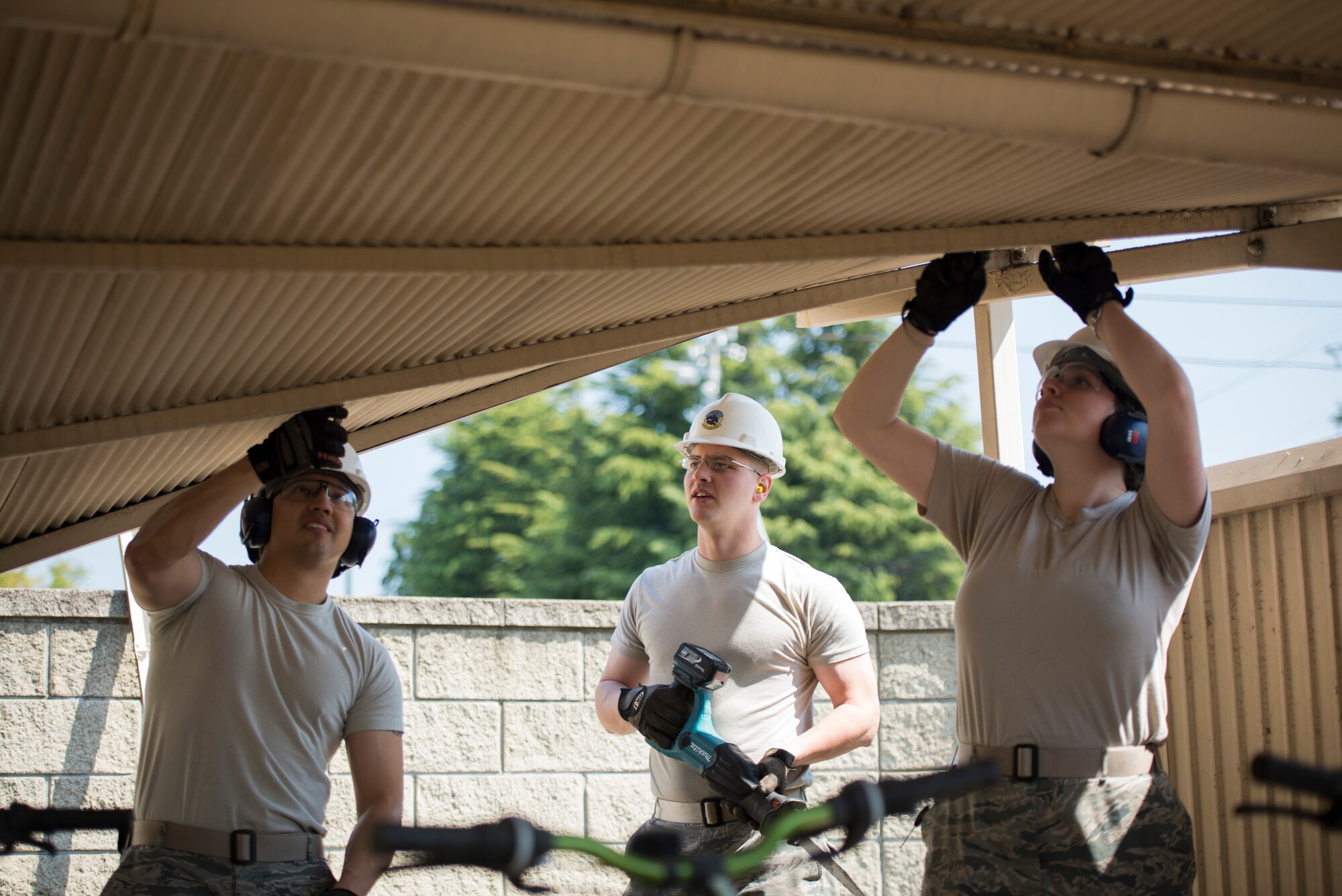 Staff Sgt. Daniel Vera-Erazo, Senior Airmen Kyle Smith and Kristen DiBennedetto remove bolts while discussing the safest route to remove a damaged roof at Yokota Air Base, Japan, April 24, 2014. The roof, which was damaged in the winter during heavy snowfall, was removed to prevent possible injury and allow dormitory residents access to their bicycle lot. The team of Airmen is with the 374th Civil Engineer Squadron structures shop. (U.S. Air Force photo by Staff Sgt. Cody H. Ramirez/Released)