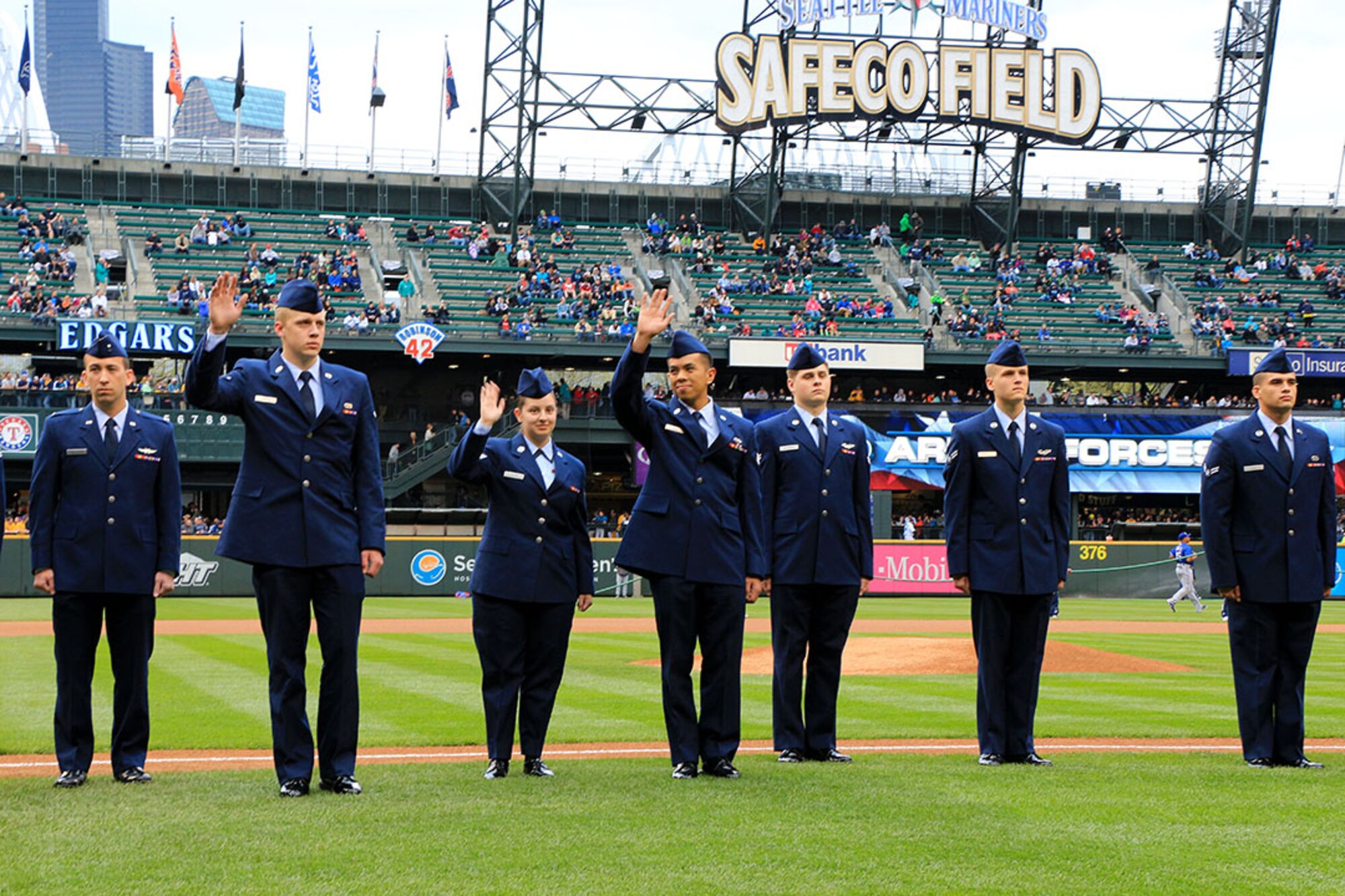 Service members stand on the Safeco Field baseline in Seattle during a pre-game ceremony for the 2014 Seattle Mariners Salute to Armed Forces Night on April 26. These service members, including three 446th Airlift Wing Reservists (waving), stood with members of the Mariners baseball team during the playing of the National Anthem. The Reservists from the 446th AW included Senior Airman Bonn Abad (right)and Airman Austin Jodzko (left) of the 446th Aircraft Maintenance Squadron and Senior Airman Sheriah Coburn (middle) of the 446th Maintenance Group. (U.S. Air Force Reserve Photo by Senior Airman Madelyn McCullough)