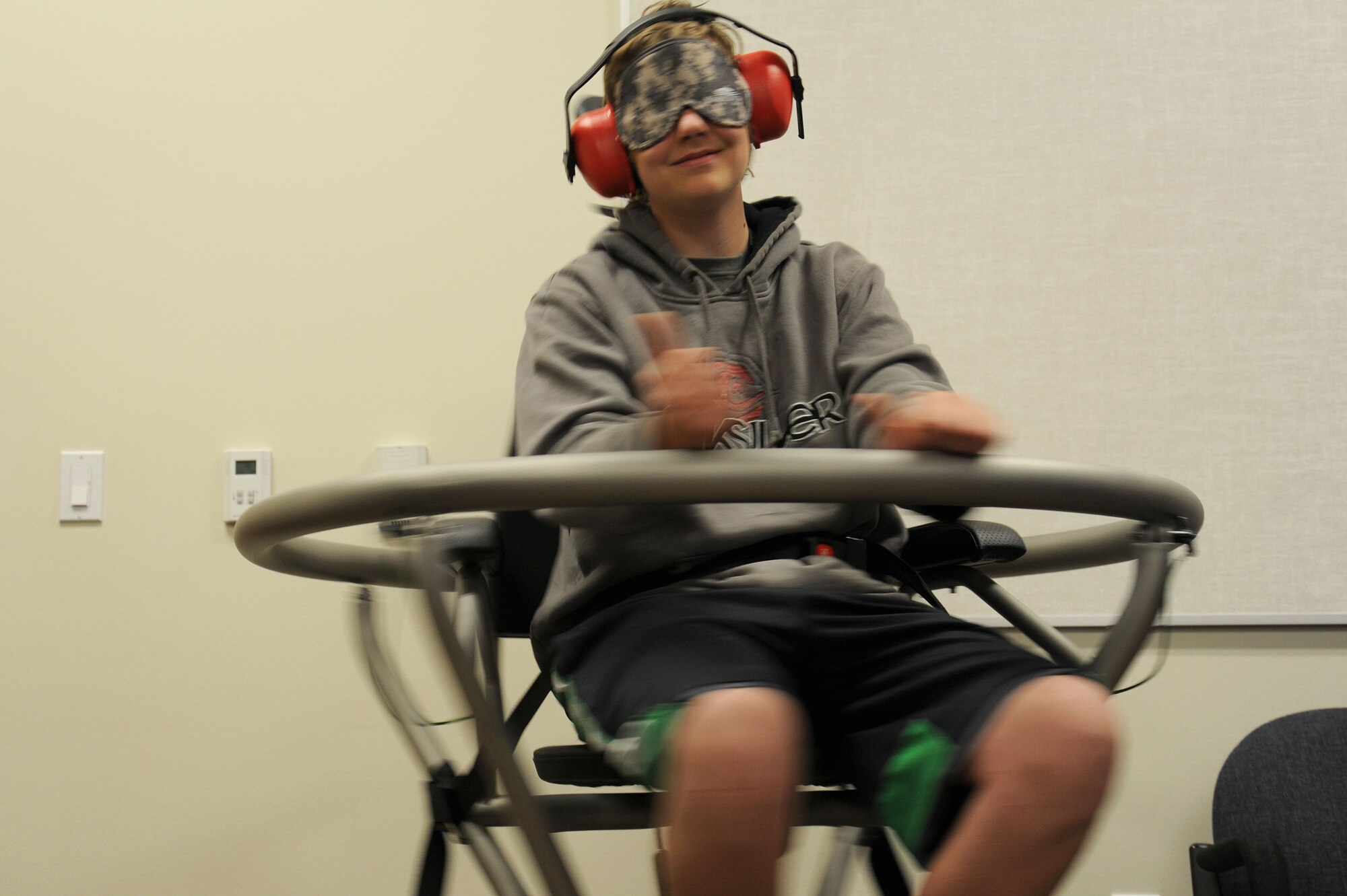 A student from Bancroft High School tries the Barany chair with his eyes and ears covered during a base tour at Fairchild Air Force Base, Wash., April 25, 2014. The Barany chair is a training tool that helps Airmen understand spatial disorientation and learn to trust their instruments. (U.S. Air Force photo by Airman 1st Class Janelle Patiño/Released)
