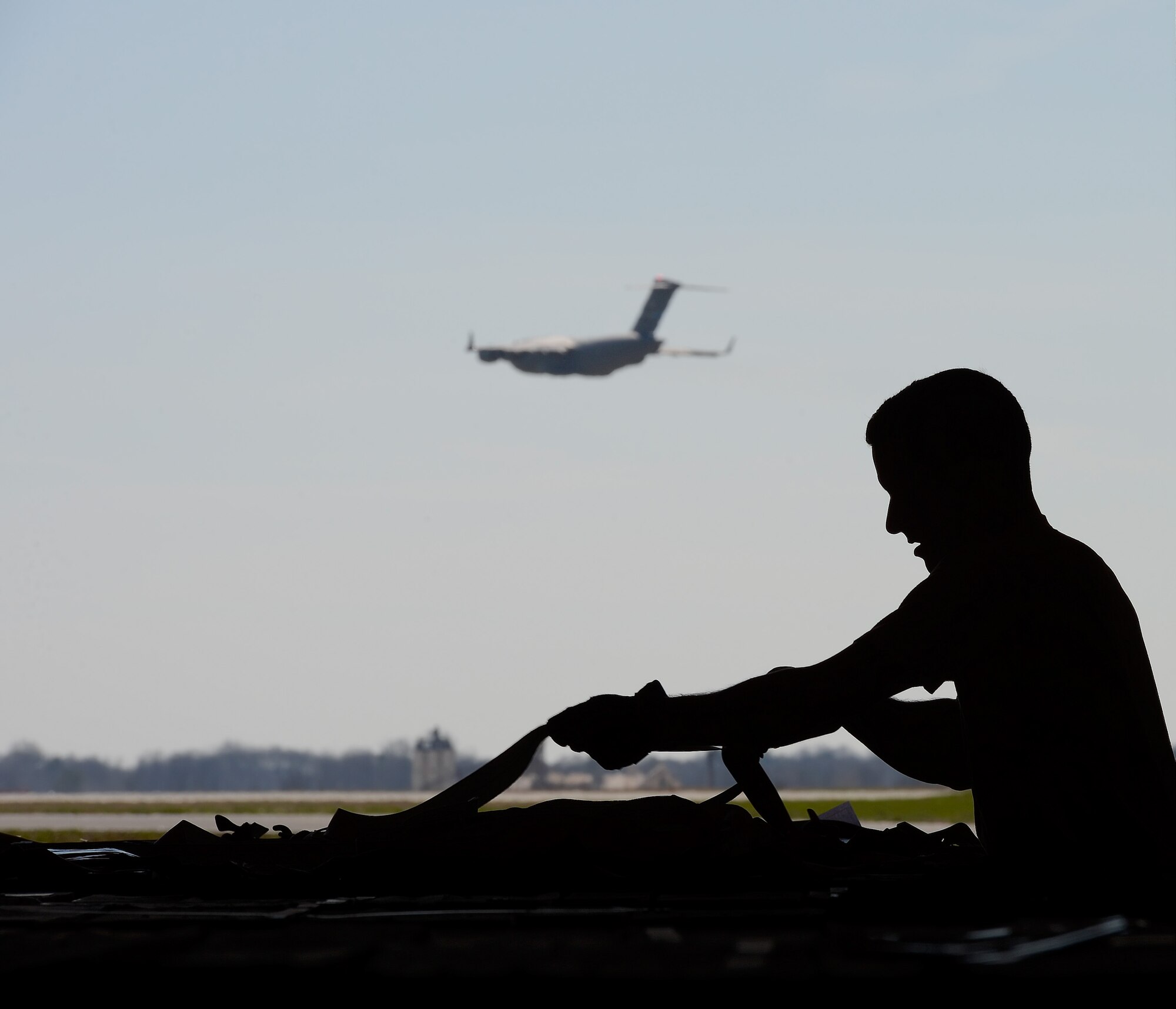 Tech. Sgt. Paul Osborn, 436th Aerial Port Squadron NCO in charge of in-transit munitions section, works to configure cargo netting over large pallets in preparation for movement and storage on April 10, 2014, at Dover Air Force Base, Del. Most of the munitions processed by the section are transported via airlift aircraft such as the C-17A Globemaster III captured in-flight in the background. (U.S. Air Force photo/Greg L. Davis)