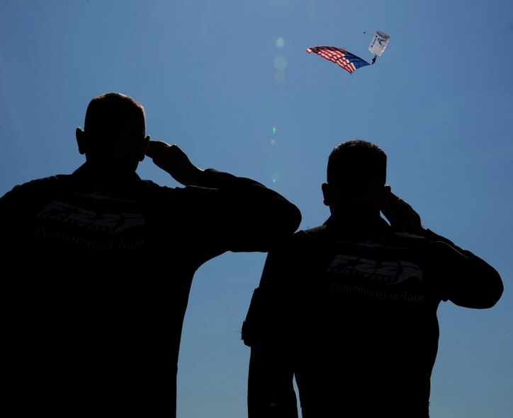 Members of the F-22 Demonstration Team salute the American Flag as a parachutist from the U.S. Air Force Sky Diving Team descends toward the ground during the Defenders of Liberty Air Show on Barksdale Air Force Base, La., April 25, 2014. The sky diving team, known as the Wings of Blue, makes roughly 19,000 jumps per year for AM490, the basic free fall course, and training, which results in approximately 700 jump wings being awarded annually. (U.S. Air Force photo/Senior Airman Joseph A. Pag?n Jr.)
