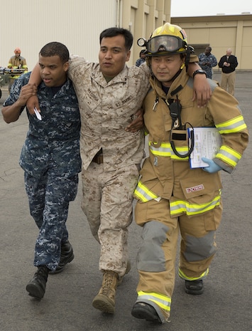 Seaman Darion Black, left, general duty corpsman with Robert M. Casey Medical and Dental Clinic, and a firefighter with the station Fire Department work together to assist Lance Cpl. David Mayorga, a patrolman with the Provost Marshal’s Office, as part of a mock scenario during a mass casualty evacuation drill on the flight line aboard Marine Corps Air Station Iwakuni, Japan, April 2, 2014.