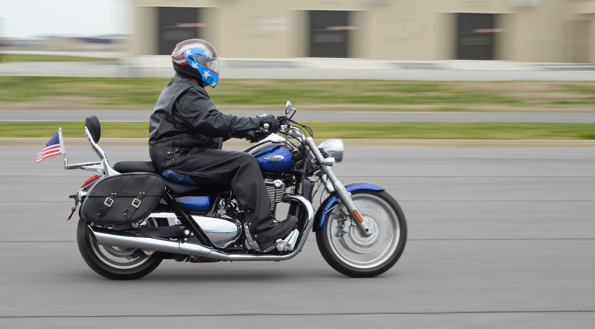 Maj. Scott Christensen, U.S. Army Reserve Sustainment Command, streaks across the motorcycle safety training range on April, 2014, at Dover Air Force Base, Del. Christensen rides a blue Triumph trimmed with chrome and sports the American flag on both the motorcycle and helmet. (U.S. Air Force photo/Greg L. Davis)