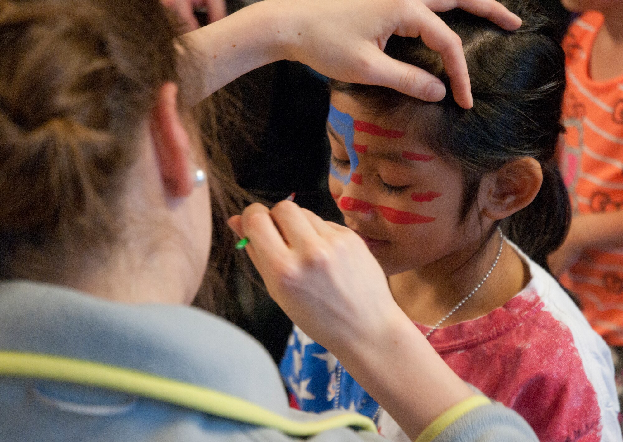 Alice Ritschard, daughter of Col. Hans Ritschard, 90th Medical Group commander, paints the face of Monica-Teresa Bersabe, 5, daughter of Capt. Carlos Bersabe, 90th Operations Support Squadron, April 25 in the Fall Hall Community Center. This is the third consecutive Military Child Bash to celebrate Month of the Military child. (U.S. Air Force photo by Airman Malcolm Mayfield)