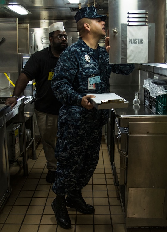 Petty Officer 3rd Class Wilson Araujo, Naval Health Clinic Charleston preventive medicine technician, talks with. Samuel Hankins, a steward cook onboard USNS Zues (T-ARC-7), about sanitation standards Apr. 25, 2014, while the ship was inport Charleston, S.C. Araujo was conducting a shipboard sanitation inspection which is required for all USNS ships to dock internationally. (U.S. Air Force photo/ Airman 1st Class Clayton Cupit)