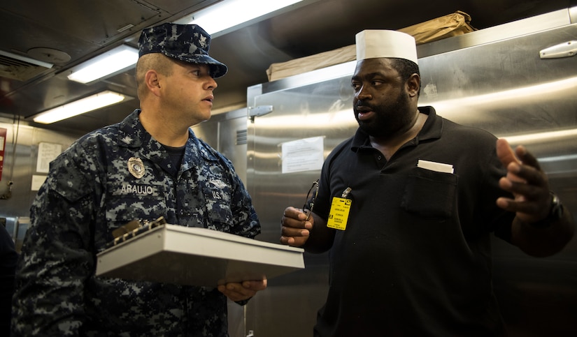 Petty Officer 3rd Class Wilson Araujo, Naval Health Clinic Charleston preventive medicine technician, talks with Samuel Hankins, a steward cook onboard USNS Zues (T-ARC-7), about sanitation standards Apr. 25, 2014, while the ship was in port Charleston, S.C. Araujo was conducting a shipboard sanitation inspection which is required for all USNS ships to dock internationally. (U.S. Air Force photo/ Airman 1st Class Clayton Cupit)