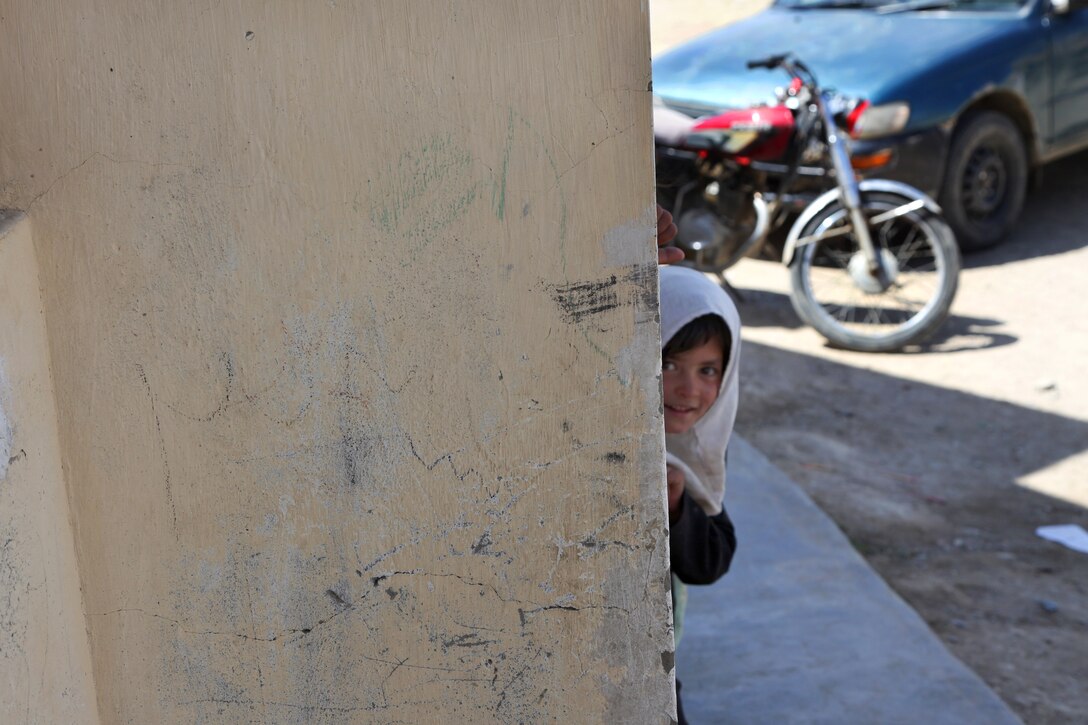 An Afghan girl peers around the corner of a building watching U.S. soldiers and an Afghan military police officer deliver supplies during a humanitarian aid event for the Qualla Bland Girls School near Bagram Airfield in Afghanistan's Parwan province, April 16, 2014.