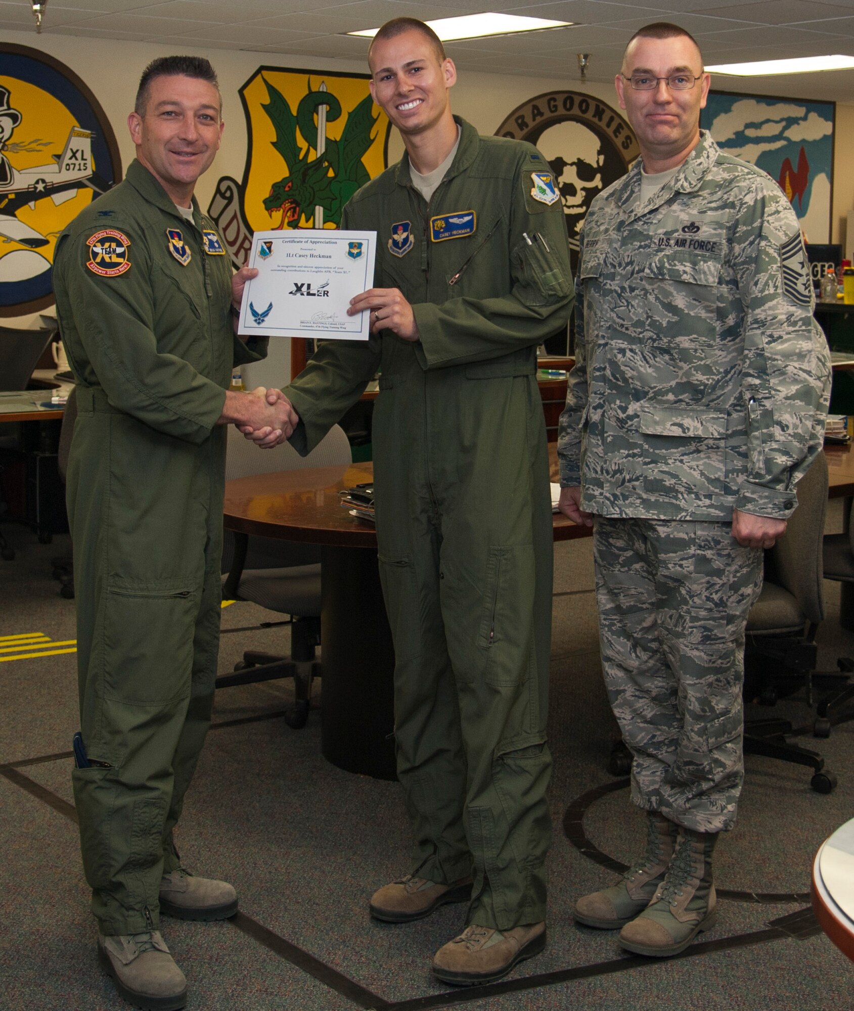 First Lt. Casey Heckman, center, 85th Flying Training Squadron T-6A Texan II instructor pilot, poses with Col. Brian Hastings, left, 47th Flying Training Wing commander, and Chief Master Sgt. Garry Berry, right, 47th FTW command chief, after being presented the XLer of the week award here April 30, 2014. The XLer is a weekly award chosen by wing leadership and given to those who consistently make outstanding contributions to their unit and Laughlin. (U.S. Air Force photo/Airman 1st Class Jimmie D. Pike/Released)