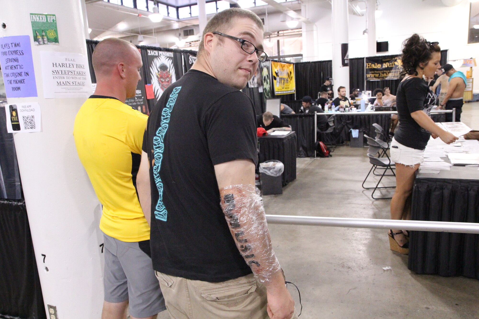 A U.S. Navy submariner, second from left, looks to the camera after getting the word "music" tattooed on his arm, at the Pacific Ink & Art Expo, Blaisdell Exhibition Hall, Honolulu, Hawaii, Aug. 4, 2013. The Navy, with one of the oldest traditions of tattooing, is thought by its sister services to have the most lenient or accepting attitude towards the decorative body art. According to AFT 36-2903, having words tattooed on the body is allowed as long as it does not violate any of the provisions regarding size, content, or placement. (U.S. Air Force photo by Tech. Sgt. Phyllis Keith)