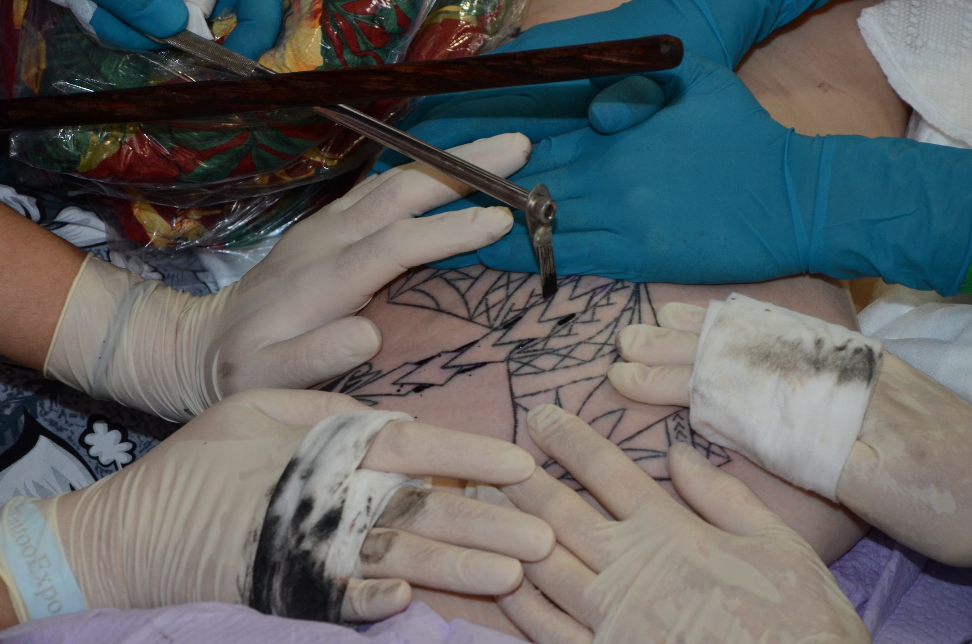 Su'a Sulu’ape Angela, a tattoo artist from San Diego, Calif., uses sterile, stainless steel tools to hand-tap a tattoo for a Marine Corps member at the Pacific Ink & Art Expo, Blaisdell Exhibition Hall, Honolulu, Hawaii, Aug. 4, 2013. This traditional Polynesian-style of body art requires assistants to stretch the skin while the ink is tapped into the skin. Angela said, “Inadvertently the way the tools were built there’s not much bleeding and it heals superfast. Military members getting a tattoo should make sure anything that will touch the skin—gloves, needles, ink cups—is single-use only. (U.S. Air Force photo by Tech. Sgt. Phyllis Keith)