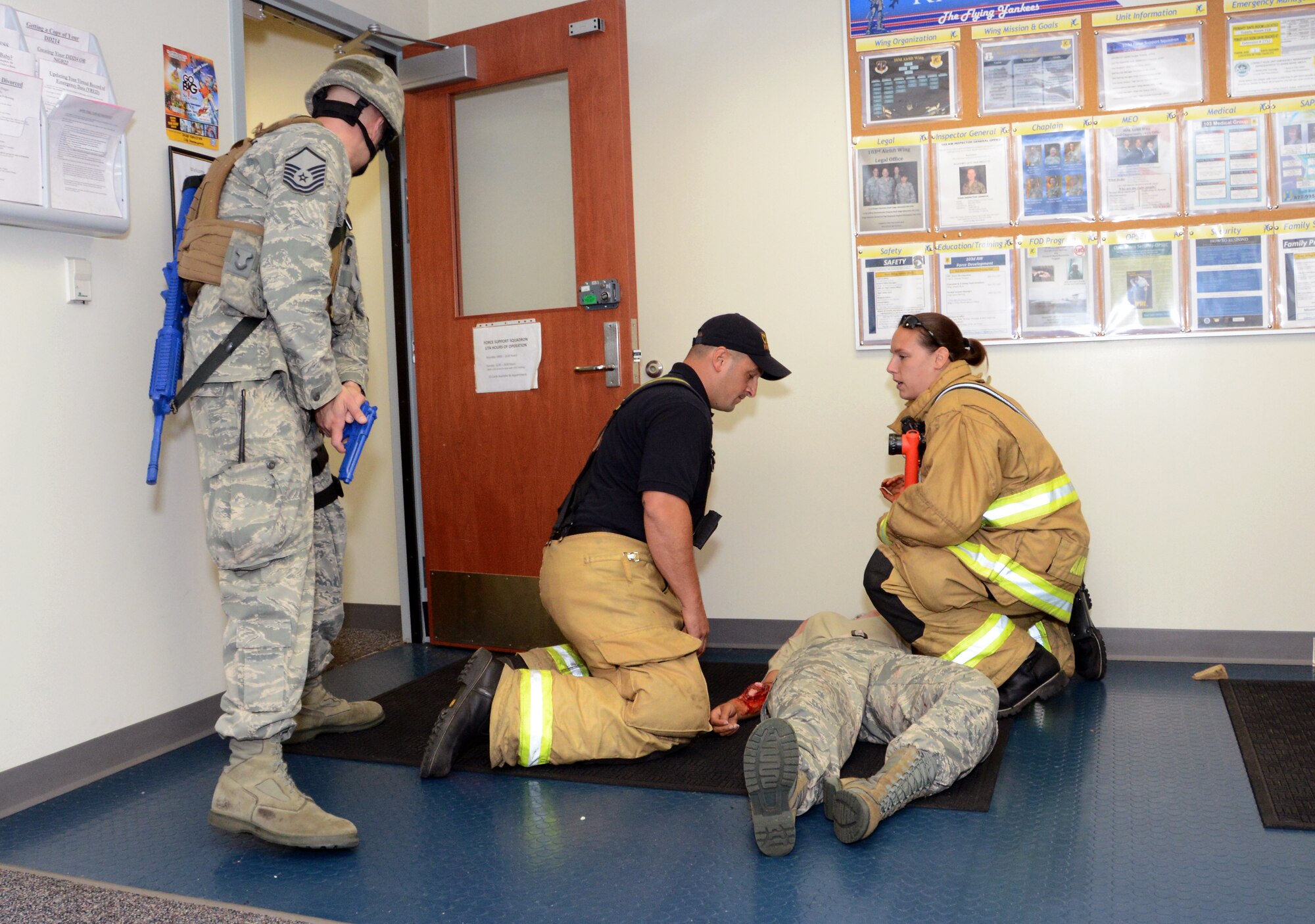 Howard Coro and Staff Sgt. Lisa Deskis, firefighters with the 103rd Civil Engineer Squadron, determine the best method of transport for Airman First Class Nathalie Jean-Louis who is depicted with simulated wounds during an active shooter exercise at Bradley Air National Guard Base in East Granby, Conn. on July 30, 2014. Master Sgt. Christopher Redo provides security for the firefighters as they tend to the wounded during the exercise. (U.S. Air National Guard photo by Tech. Sgt. Joshua Mead/Released)