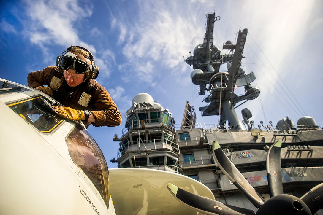 U.S. Navy Petty Officer 3rd Class Robert Tindell cleans an E-2C Hawkeye's windshield on the flight deck of the aircraft carrier USS George Washington east of Okinawa, July 30, 2014. The Washington and its embarked air wing, Carrier Air Wing 5, provide a combat-ready force that protects and defends the maritime interests of the U.S. and its allies and partners in the Indo-Asia-Pacific region. The Hawkeye is assigned to Airborne Early Warning Squadron 115. 