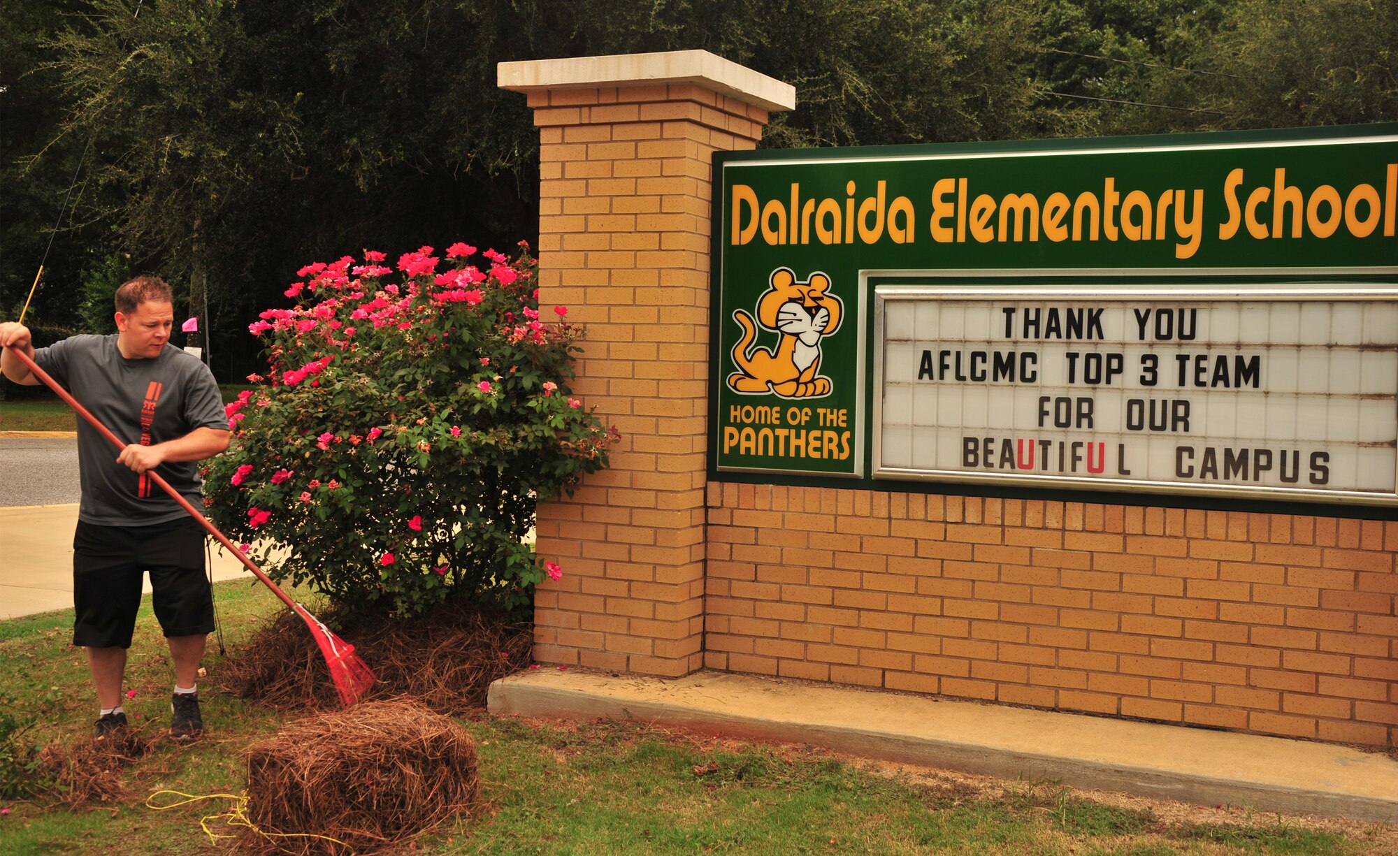 Tech. Sgt. Phillip Gardner, Air Force Life Cycle Management Center network infrastructure manager, rakes loose landscaping around the Dalraida Elementary School sign Aug. 1, 2014. Members of the AFLCMC  at Maxwell’s Gunter annex volunteered to clean-up the grounds at Dalraida Elementary School in Montgomery, Ala. The volunteer effort, organized by the AFLCMC Top 3, dubbed a “beautification project” included 25 military personnel doing general grounds maintenance. (U.S. Air Force photo by/Staff Sgt. Erica Picariello)