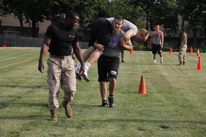 Eric W. Naulty, a junior Blue Valley Northwest High School Huskies offensive guard and defensive tackle, fireman carries Jack J. Kutey, a senior Huskies defensive end, as Sgt. Laronald R. McKinney, a Marine Corps Recruiting Station Kansas City, Recruiting Sub-Station Olathe recruiter, encourages Naulty to push through at the Huskies' practice field Aug. 5, 2014 during the Combat Fitness Test. The fireman carry makes up the maneuver-under-fire portion of the CFT and participants must perform pushups, a high and low crawl, cone-agility drills, a buddy drag, throw a dummy grenade, and finish with a sprint, carrying 30-pound ammunition cans. 