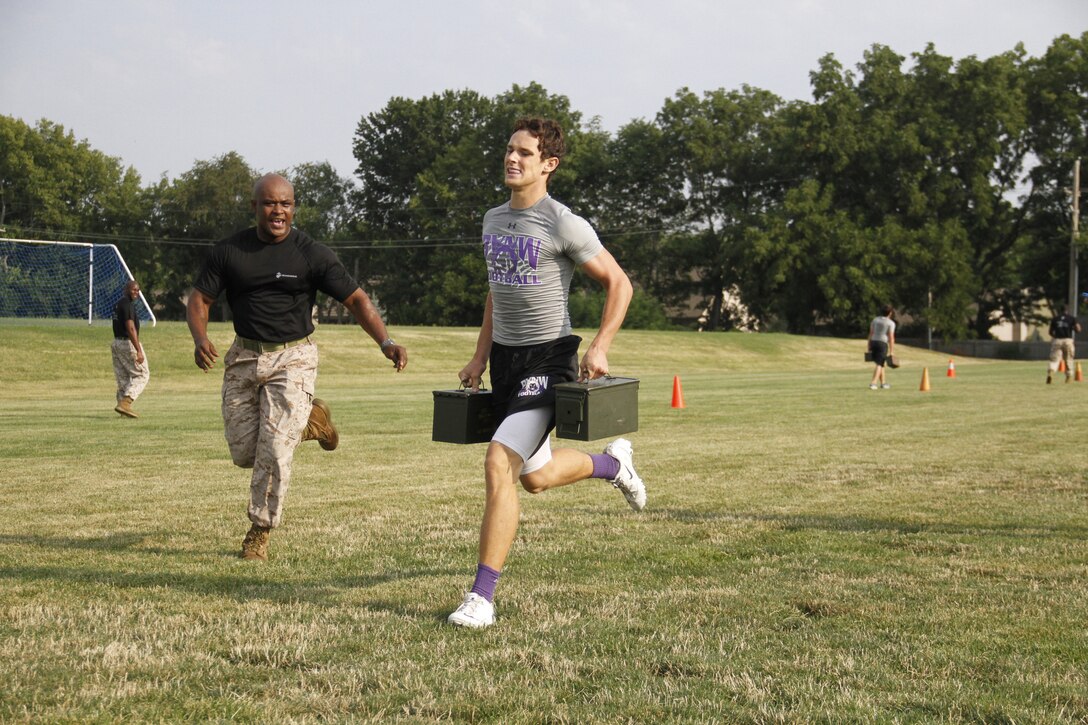 Zack D. Zegunis, a senior Blue Valley Northwest High School Huskies quarterback and free safety, sprints to the finish line with two 30-pound ammunition cans as Staff Sgt. Reginald Jacques, Marine Corps Recruiting Station Kansas City's administration chief, yells motivation during the Combat Fitness Test at the Huskies' practice field Aug. 5, 2014. Marines from both RS Kansas City and Recruiting Sub-Station Olathe were on hand to monitor and motivate the players throughout the event.