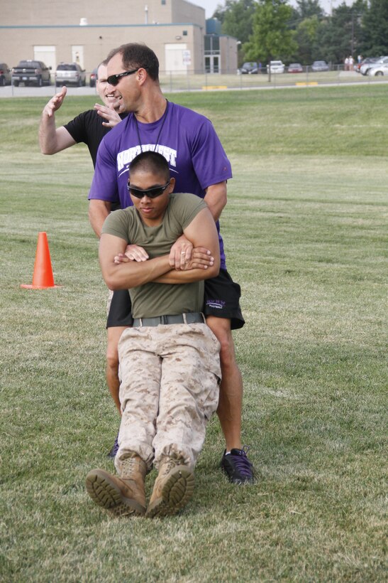 Mike H. Zegunis, the Blue Valley Northwest High School Huskies' head football coach, buddy drags Lance Cpl. Dominic P. Ehretmounivong, a Detachment 2, Supply Company, Combat Logistics Battalion 453 warehouse clerk, to demonstrate the proper way to buddy drag to his players as Staff Sgt. Paul D. Bush, background, the Marine Corps Recruiting Station Kansas City, Recruiting Sub-Station Olathe staff noncomissioned officer-in-charge, advises on proper technique at the Huskies' practice field Aug. 5, 2014. 
