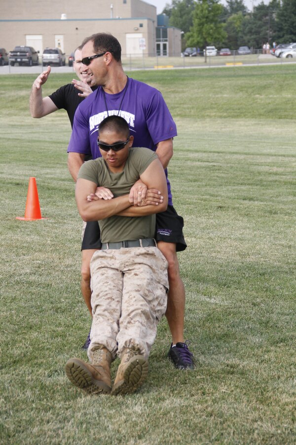 Mike H. Zegunis, the Blue Valley Northwest High School Huskies' head football coach, buddy drags Lance Cpl. Dominic P. Ehretmounivong, a Detachment 2, Supply Company, Combat Logistics Battalion 453 warehouse clerk, to demonstrate the proper way to buddy drag to his players as Staff Sgt. Paul D. Bush, background, the Marine Corps Recruiting Station Kansas City, Recruiting Sub-Station Olathe staff noncomissioned officer-in-charge, advises on proper technique at the Huskies' practice field Aug. 5, 2014. 