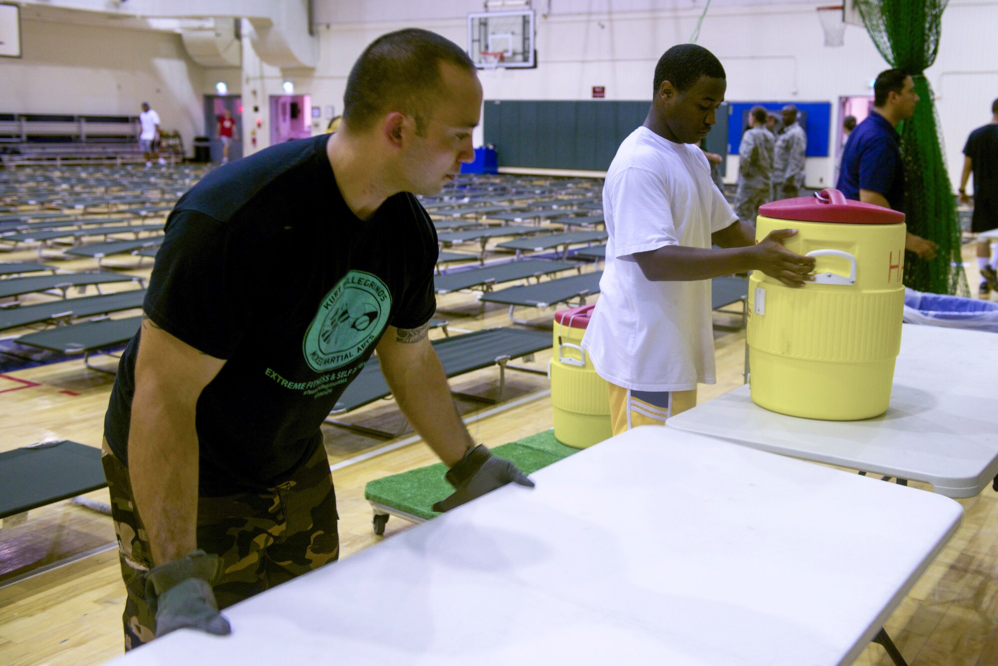 Volunteers from Yokota Air Base, Japan prepare the Samurai Fitness Center to host nearly 200 passengers whose flight was delayed by a weather contingency in Okinawa, Japan on Aug. 1, 2014. The volunteers set up cots, installed fans and readied water coolers in preparation. (U.S. Air Force photo by Airman 1st Class David C. Danford/Released)