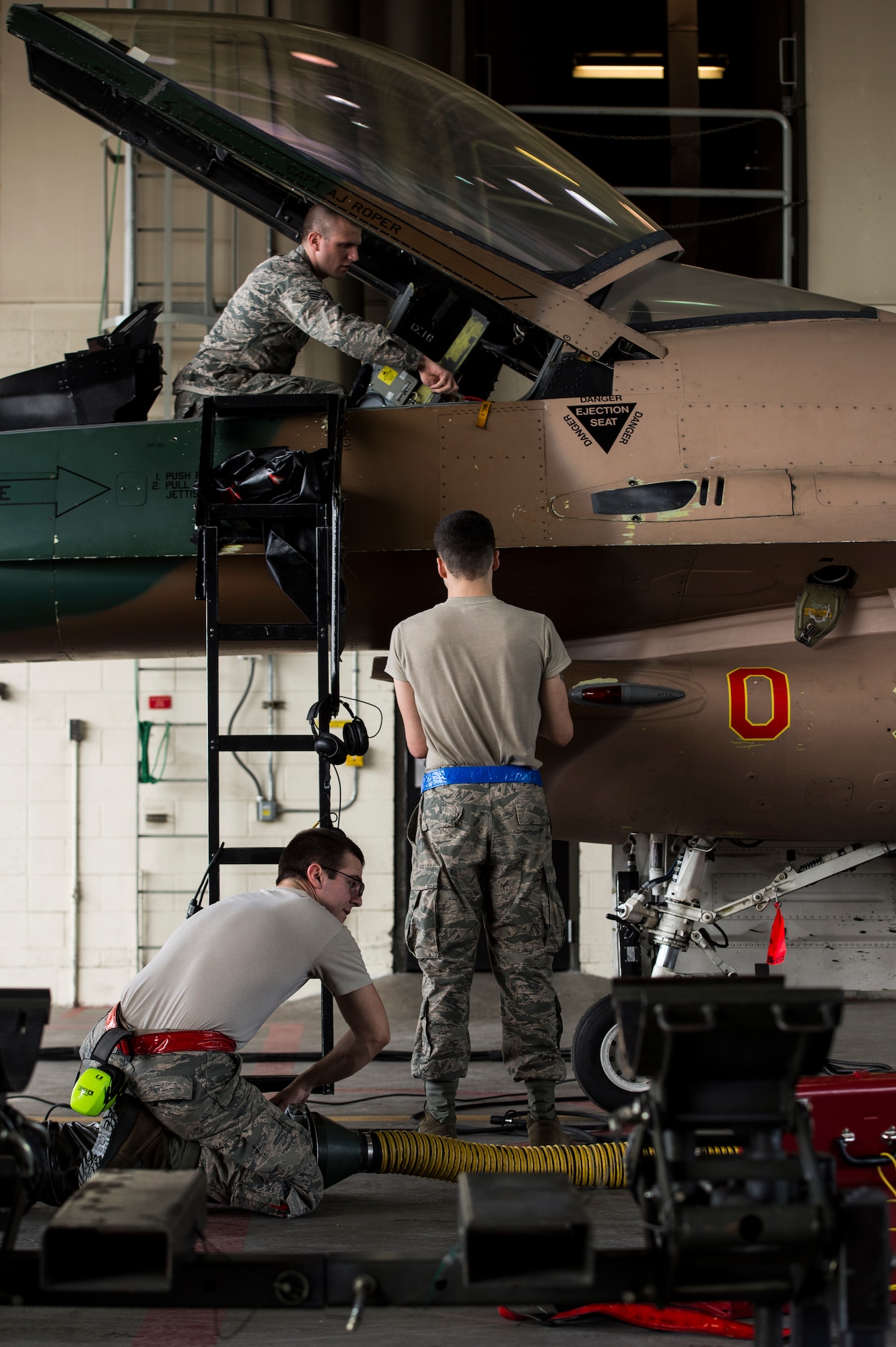 Staff Sgt. Joshua Adkins and Airman 1st Class Jesse Butler, 354th Aircraft Maintenance Squadron egress, remove a parachute while Airman 1st Class Lawrence Croby, 354th AMS weapons load crew, repairs the weapons systems on an F-16C Fighting Falcon at Eielson Air Force Base, Alaska, Aug. 4, 2014. The 354th AMS provides mission ready mission ready aircraft to support the wing's F-16 aggressor mission that includes home station, the exercise RED FLAG-Alaska and Aggressor road shows. (U.S. Air Force photo by Staff Sgt. Stephany Richards/ Released)