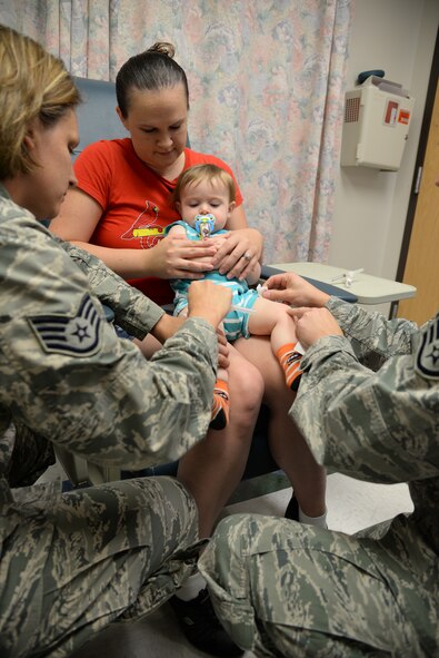 U.S. Air Force Staff Sgt. Cynthia Reichardt, 23d Medical Operations Squadron NCO in charge of allergy and immunizations, left, and Staff Sgt. Matthew Scully, 38th Rescue Squadron independent duty medical technician, place adhesive bandages on Elliot Watts, son of Staff Sgt. Sean Watts,  after being vaccinated at Moody Air Force Base, Ga., July 30, 2014. Moody’s immunizations clinic provides adult and pediatric routine immunizations as well as deployment and travel vaccines.(U.S. Air Force photo by Airman 1st Class Sandra Marrero/Released)  
