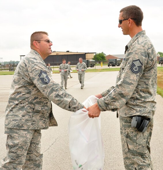 Master Sgt. Robert Watkins, 932nd Maintenance Group, Quality Assurance Inspector, collects a bag of debris collected during a routine "foreign object damage" walk from, Senior Master Sgt. Todd Wadkins, 932nd Ground and weapons safety NCO, on Scott Air Force Base, Aug 5, 2014. The FOD walk is done to help prevent mishaps with aircraft, and protect assets and mission capabilities. (U.S. Air Force photo / Staff Sgt. Amber Hodges)