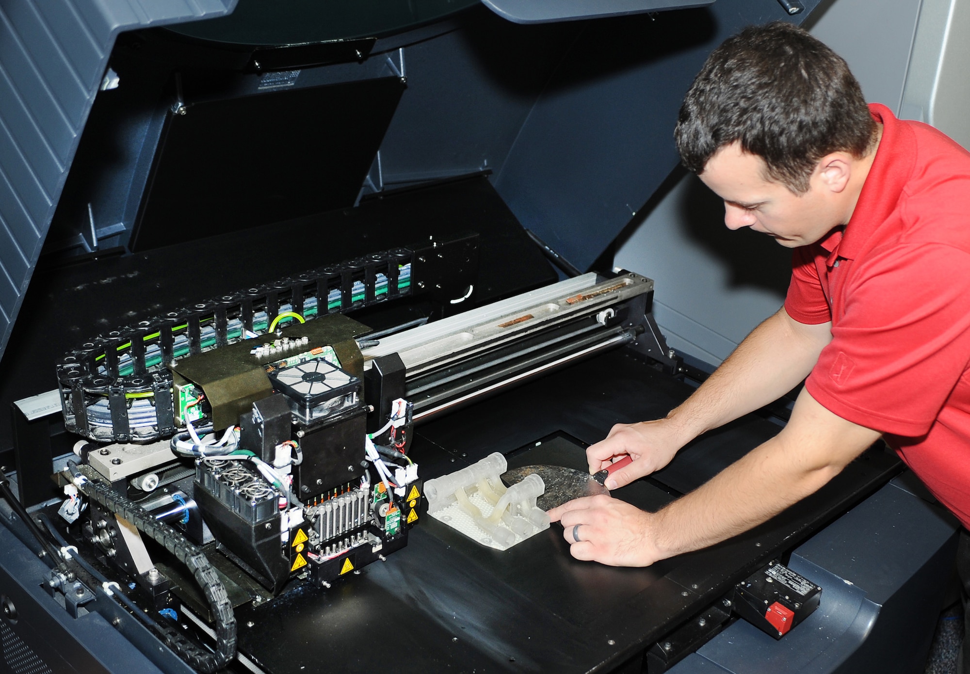 An engineer removes a 3D printed hydraulic manifold from the 3D printer July 24, 2014, at Joint Base McGuire-Dix-Lakehurst, N.J. (U.S. Navy photo/Released)