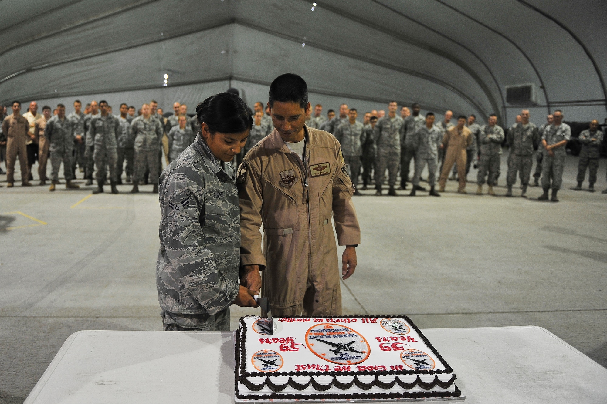 Brig. Gen. John T. Quintas, 380th Air Expeditionary Wing commander, and Airman First Class Sabrina Fisher, a 380th Expeditionary Aircraft Maintenance Squadron tactical aircraft maintenance journeyman, cut the first slice of cake at the U-2 anniversary celebration Aug. 1, 2014, at an undisclosed location in Southwest Asia. The celebration marked the 59th anniversary of the aircraft. (U.S. Air Force photo by Tech. Sgt. Russ Scalf/Released)