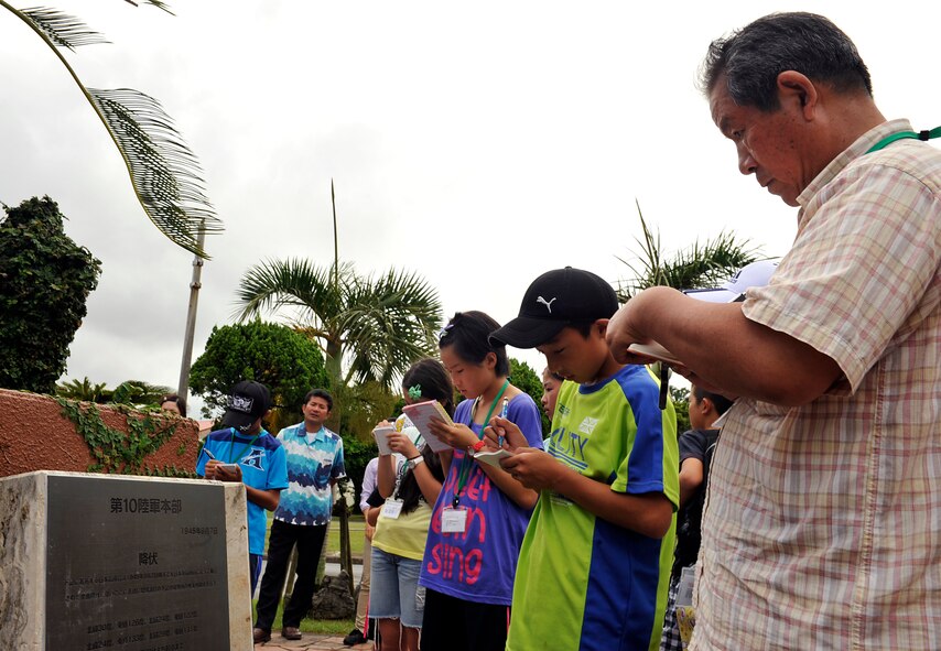 Keima Okaniwa, Achi Village, Nagano "chimuzawa" (cultural exchange) association director (right), and primary school children from Achi Village, Nagano, take notes in front of a plaque at the Peace Garden memorial during a visit on Kadena Air Base, Japan, Aug. 4, 2014. This is the 11th annual Okinawa visit and eighth straight year that children visited Kadena. The children visited several facilities and engaged with American children their age during the visit. (U.S. Air Force photo by Naoto Anazawa/Released)