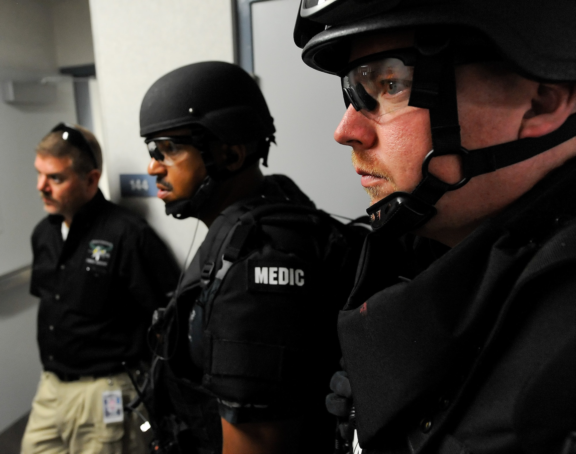 Three members of the Kent County, Delaware, Department of Public Safety, Division of Emergency Medical Services, listen intently during a briefing in a hallway as they respond to a Major Accident Response Exercise with active shooter scenario on Aug. 1, 2014, at Dover Air Force Base, Del. From right to left are: Rich Allen, Scott McMillon, both tactical medics, and Capt. John Tinger, SWAT Medical Team commander. (U.S. Air Force photo/Greg L. Davis)