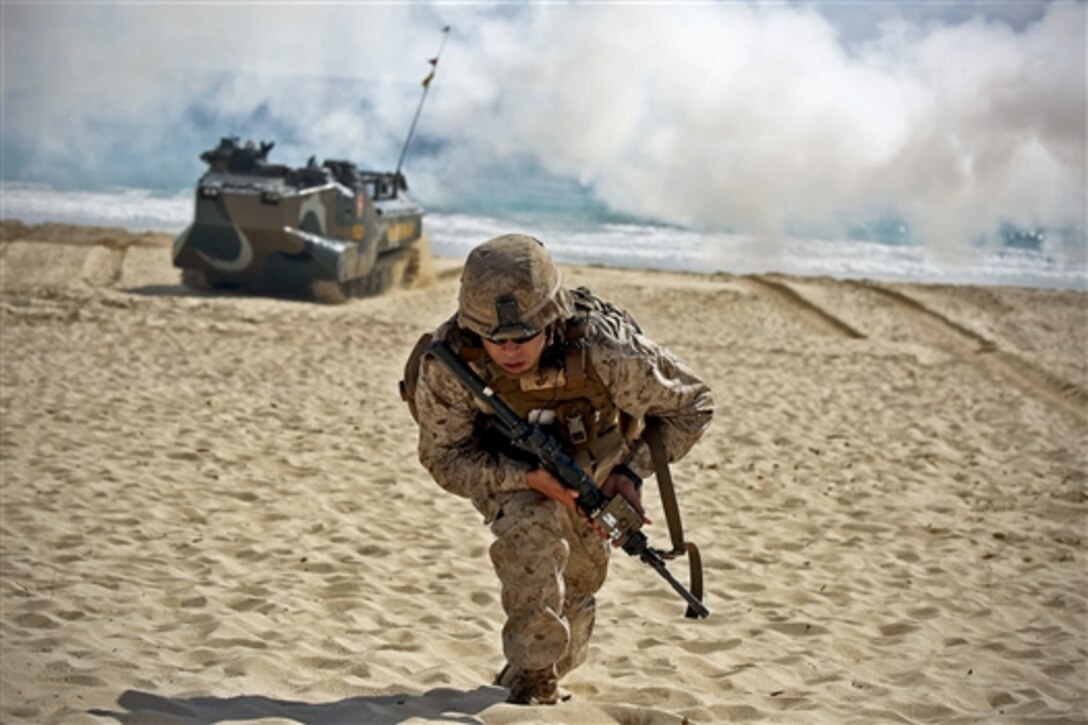 A Marine runs forward while an amphibious assault vehicle drives onto the sand behind him on Pyramid Rock Beach on Marine Corps Base Hawaii, July 29, 2014, as part of the final assault during the Rim of the Pacific 2014. The exercise involves 22 nations, more than 40 ships and submarines, about 200 aircraft and 25,000 people. The Marine is assigned to 3rd Battalion, 3rd Marine Regiment. 