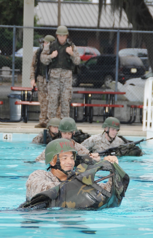 Master Sgt. Mark Carabello (front) operations and training chief, S-3, Operations and Training Division, Marine Corps Logistics Base Albany, sheds his gear and uses it as a floatation device during the annual swim qualification at the Base Pool, Aug. 1.
