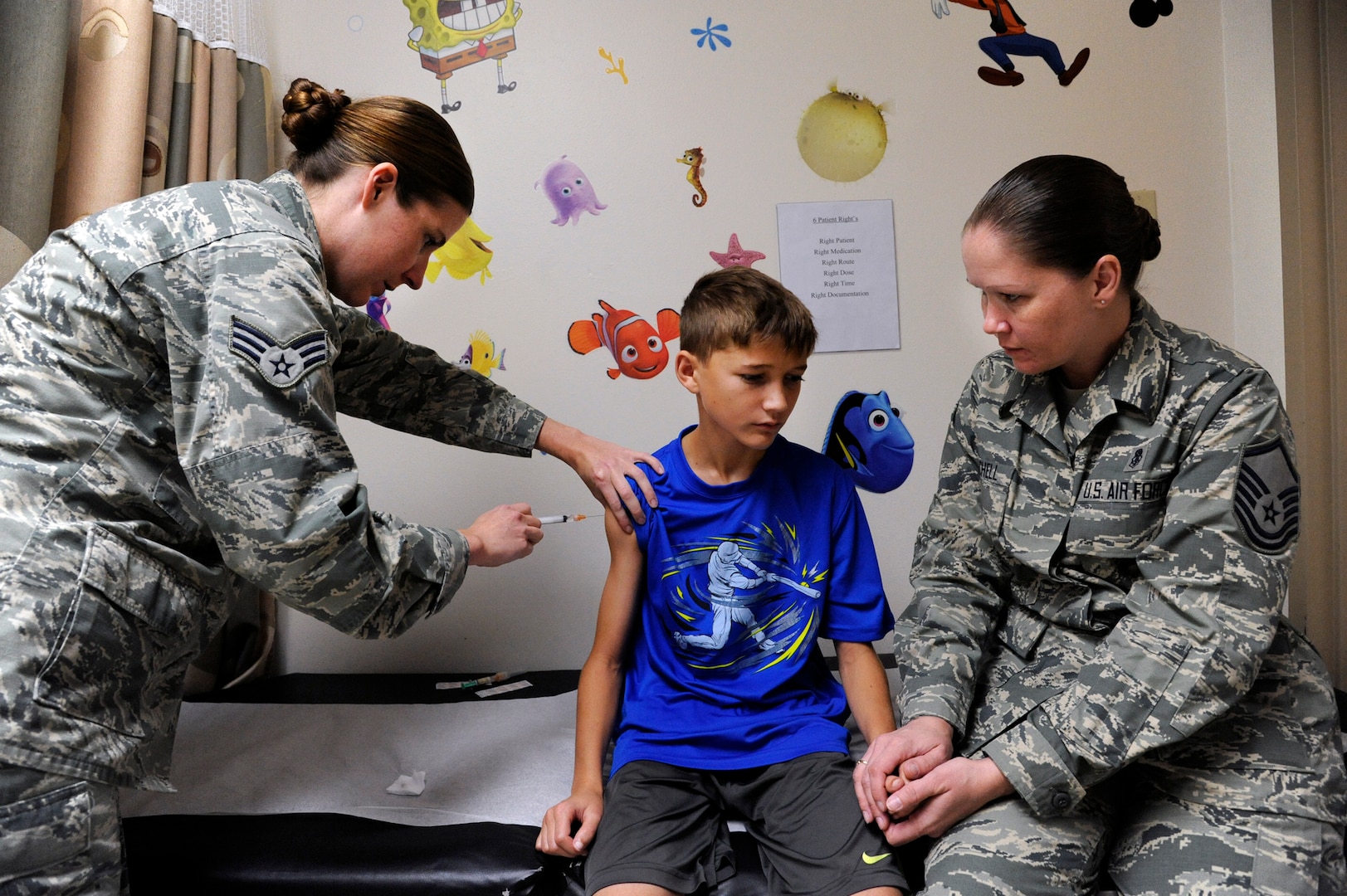 Senior Airman Kelly Boos, left, administers multiple vaccinations to Andrew Mitchell Aug. 6, 2014, as his mother, Master Sgt. Kimberly Mitchell, right, holds his hand at the Joint Base San Antonio Immunizations Clinic.. Boos is an aerospace medical technician and Mitchell is the NCO in charge at the ear, nose and throat clinic. (U.S. Air Force photo/Desiree N. Palacios)
