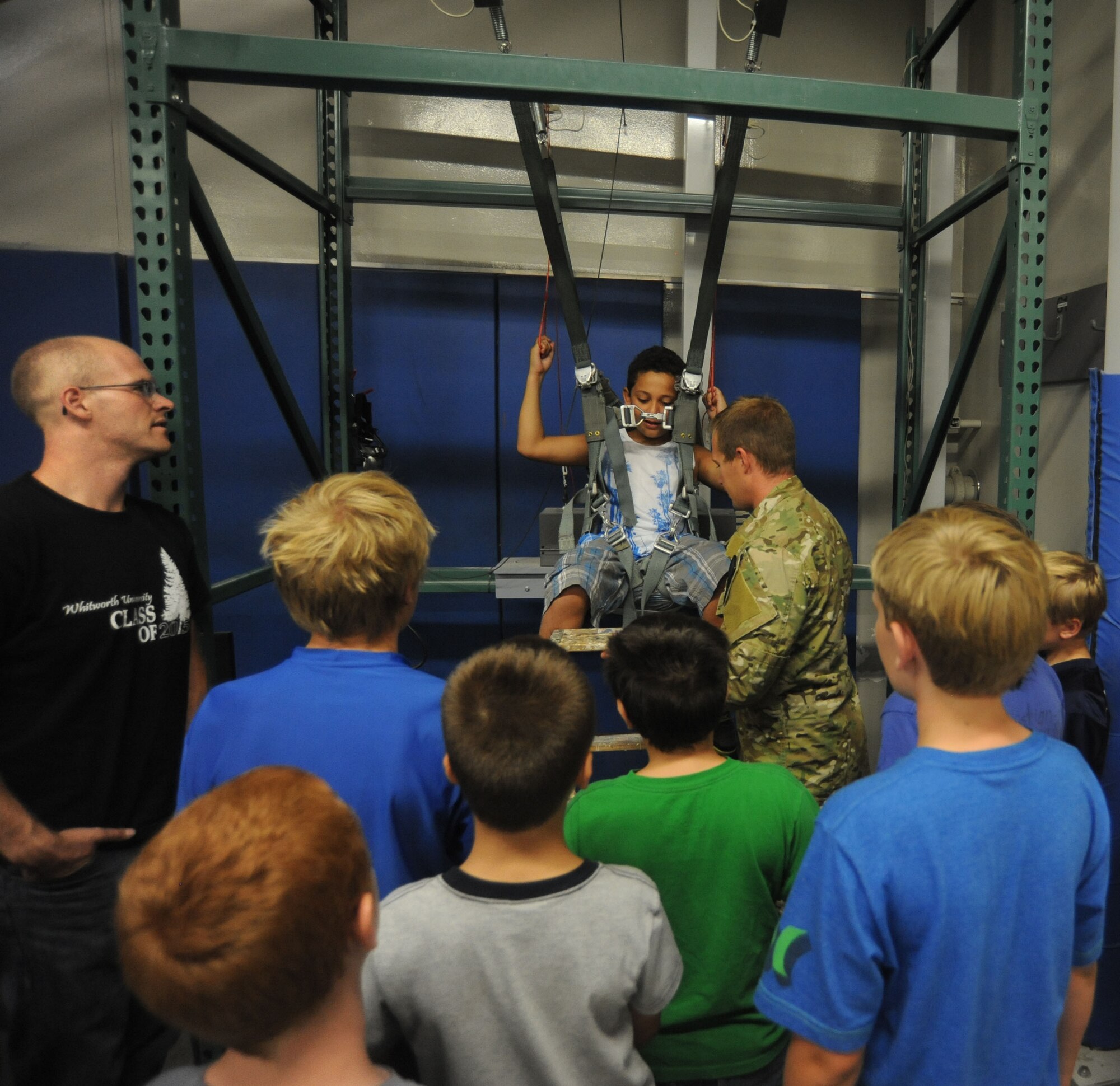 Tech. Sgt. Bon Strout installs a child from the Northeast Youth Center of Spokane summer camp into a parachute simulator at Fairchild Air Force Base, Washington, Aug. 1, 2014. Strout is with the 22nd Training Squadron. The children were on a tour of the base’s Survival, Evasion, Resistance and Escape facilities for their military theme week. (U.S. Air Force photo by Airman 1st Class Sam Fogleman/Released)