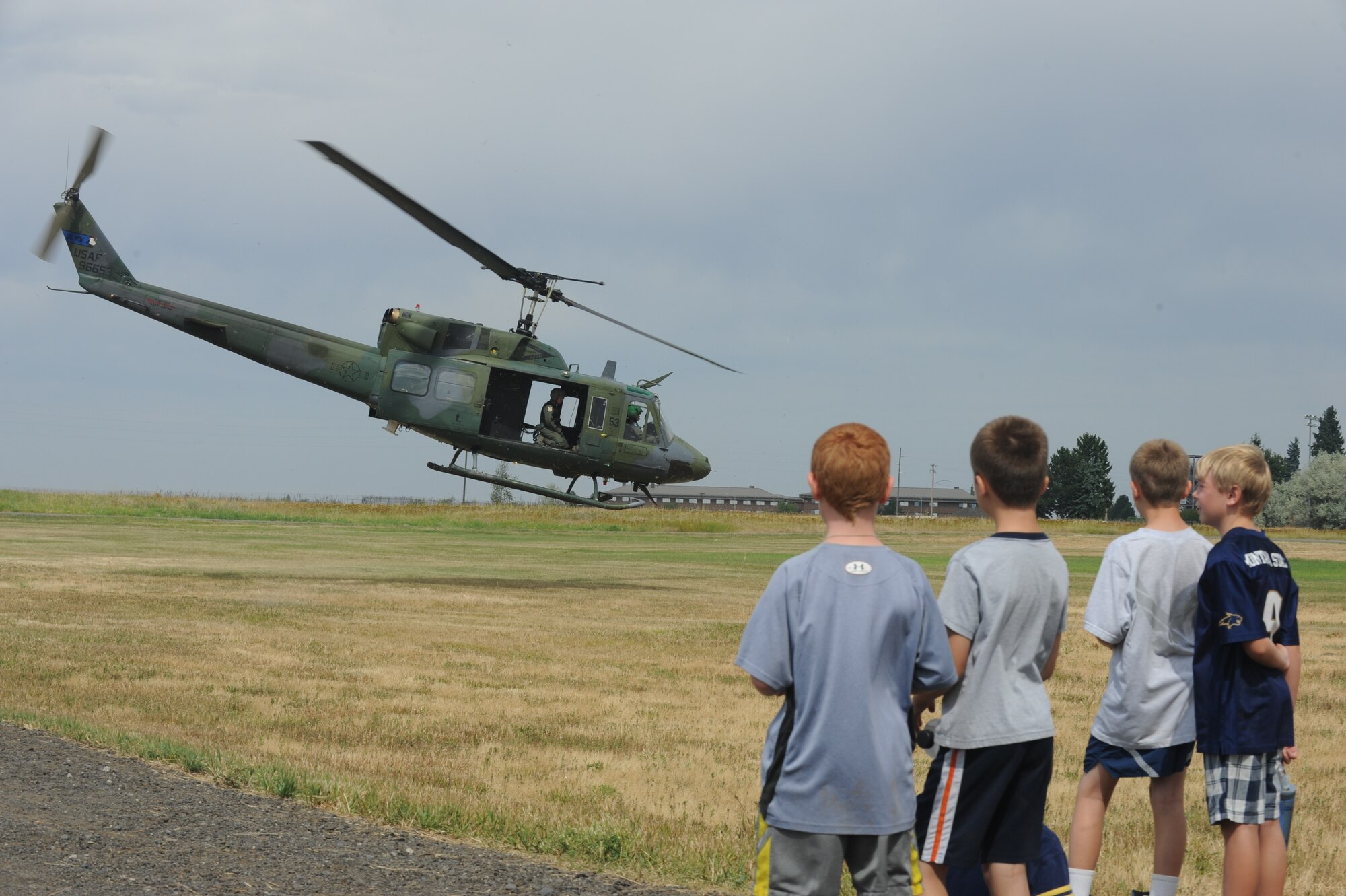 Children from the Northeast Youth Center of Spokane summer camp watch a flyby of a UH-1N Iroquois at Fairchild Air Force Base, Washington, Aug. 1, 2014. The helicopter was being flown by Airmen of the 336th Training Group. The children were on a tour of Fairchild’s Survival School to experience military missions. (U.S. Air Force photo by Airman 1st Class Sam Fogleman/Released)