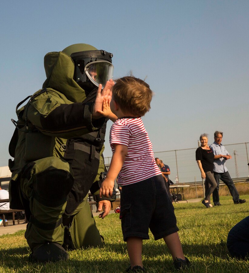 A Marine with the second iteration of SP-MAGTF Africa 14 gives a child a high-five while wearing a bomb suit at the National Night Out event aboard Naval Air Station Sigonella, Italy, Aug. 5, 2014. Marines and Sailors with SP-MAGTF Africa participated in the event with a static display of weapons, an Explosive Ordnance Disposal robot, and two vehicles organic to the Marine Corps. SP-MAGTF Africa continues to build relationships with the community while simultaneously strengthening U.S. Africa Command and U.S. Marine Corps Forces Africa’s ability to assist partner nations in addressing security challenges in the region. (U.S. Marine Corps photo by Cpl. Shawn Valosin)