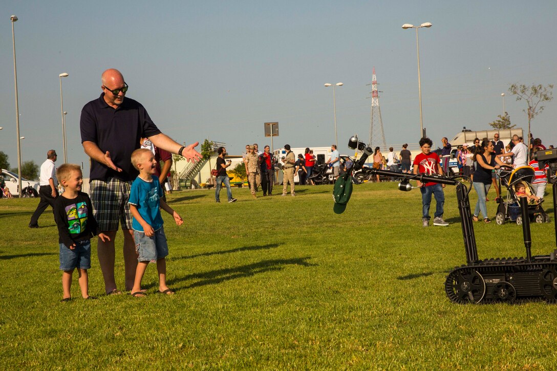 Two children are elated by an Explosive Ordnance Disposal robot during the National Night Out event aboard Naval Air Station Sigonella, Italy, Aug. 5, 2014. Their father handed the robot his hat, and then the robot gingerly took the hat, demonstrating the dexterity of the machine. Marines and Sailors with the second iteration of SP-MAGTF Africa 14 participated in the event with a static display of weapons, an Explosive Ordnance Disposal robot, and two vehicles organic to the Marine Corps. SP-MAGTF Africa continues to build relationships with the community while simultaneously strengthening U.S. Africa Command and U.S. Marine Corps Forces Africa’s ability to assist partner nations in addressing security challenges in the region. (U.S. Marine Corps photo by Cpl. Shawn Valosin)