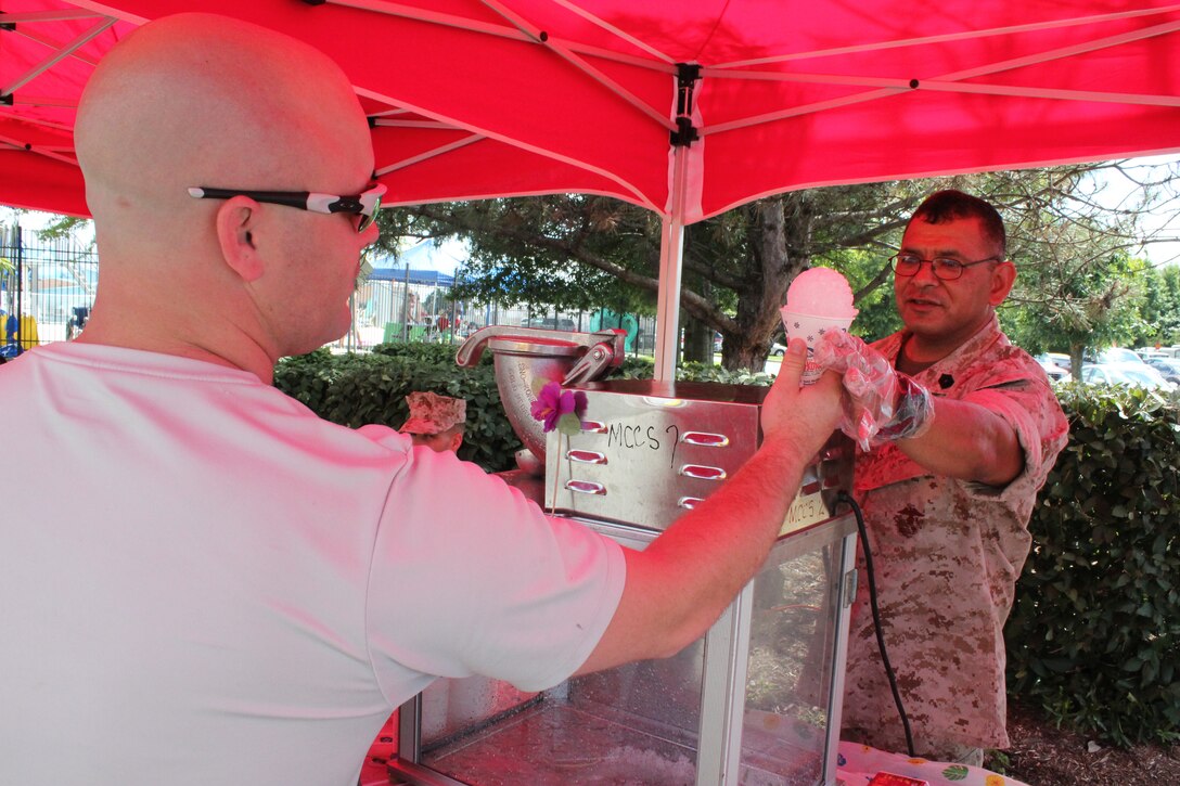 Master Sgt. Josue Santoyo, operations chief for Marine Corps Base Quantico, passes a snow cone to a Marine attending Headquarters and Service Battalion’s “Pool Bash” at the Quantico 50M Pool on July 28.