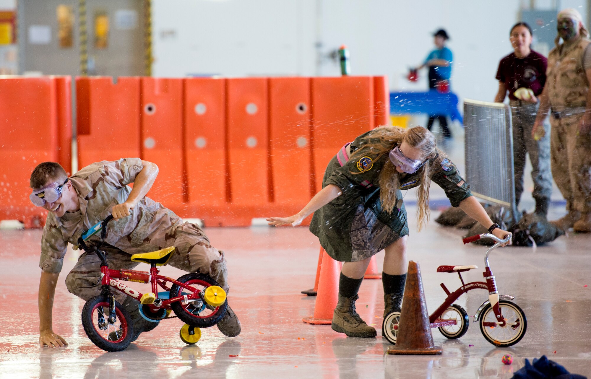 Tech. Sgt. Noah Stamps, 432nd Wing NCO in charge of chapel operations, left, and 1st Lt. Kimberly Anderson, 432nd Aircraft Communications Squadron Systems Maintenance Unit assistant officer in charge, fall off their tricycles while navigating an obstacle course during the inaugural combat dining-in at Creech Air Force Base, Nev., July 11, 2014. The combat dining-in is an 84-year-old Air Force tradition which aims to enhance espirit de corps and build camaraderie with fellow Airmen. (U.S. Air Force photo by Tech. Sgt. Shad Eidson/Released)