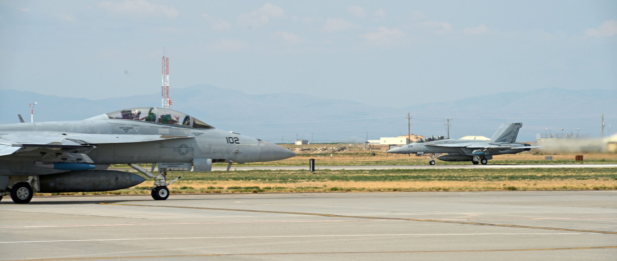 A F-18F Super Hornet, assigned to VFA 154 Naval Air Station Lemoore, Calif., taxis on the runway Aug. 5, 2014, at Mountain Home Air Force Base, Idaho, while another F-18F Super Hornet takes off behind it. The VFA 154 aircrews have been acting as Red Force during combat training scenarios against 389th Fighter Squadron [Blue Force] aircraft while here. (U.S. Air Force photo by Senior Airman Benjamin Sutton/Released)