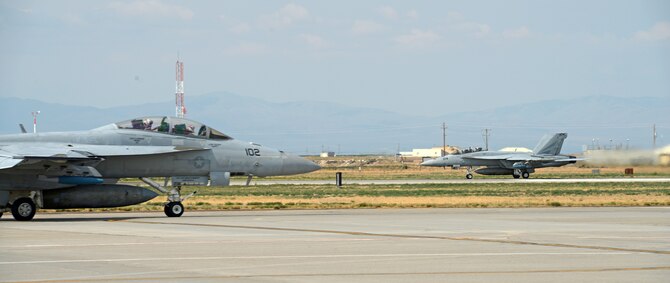 A F-18F Super Hornet, assigned to VFA 154 Naval Air Station Lemoore, Calif., taxis on the runway Aug. 5, 2014, at Mountain Home Air Force Base, Idaho, while another F-18F Super Hornet takes off behind it. The VFA 154 aircrews have been acting as Red Force during combat training scenarios against 389th Fighter Squadron [Blue Force] aircraft while here. (U.S. Air Force photo by Senior Airman Benjamin Sutton/Released)