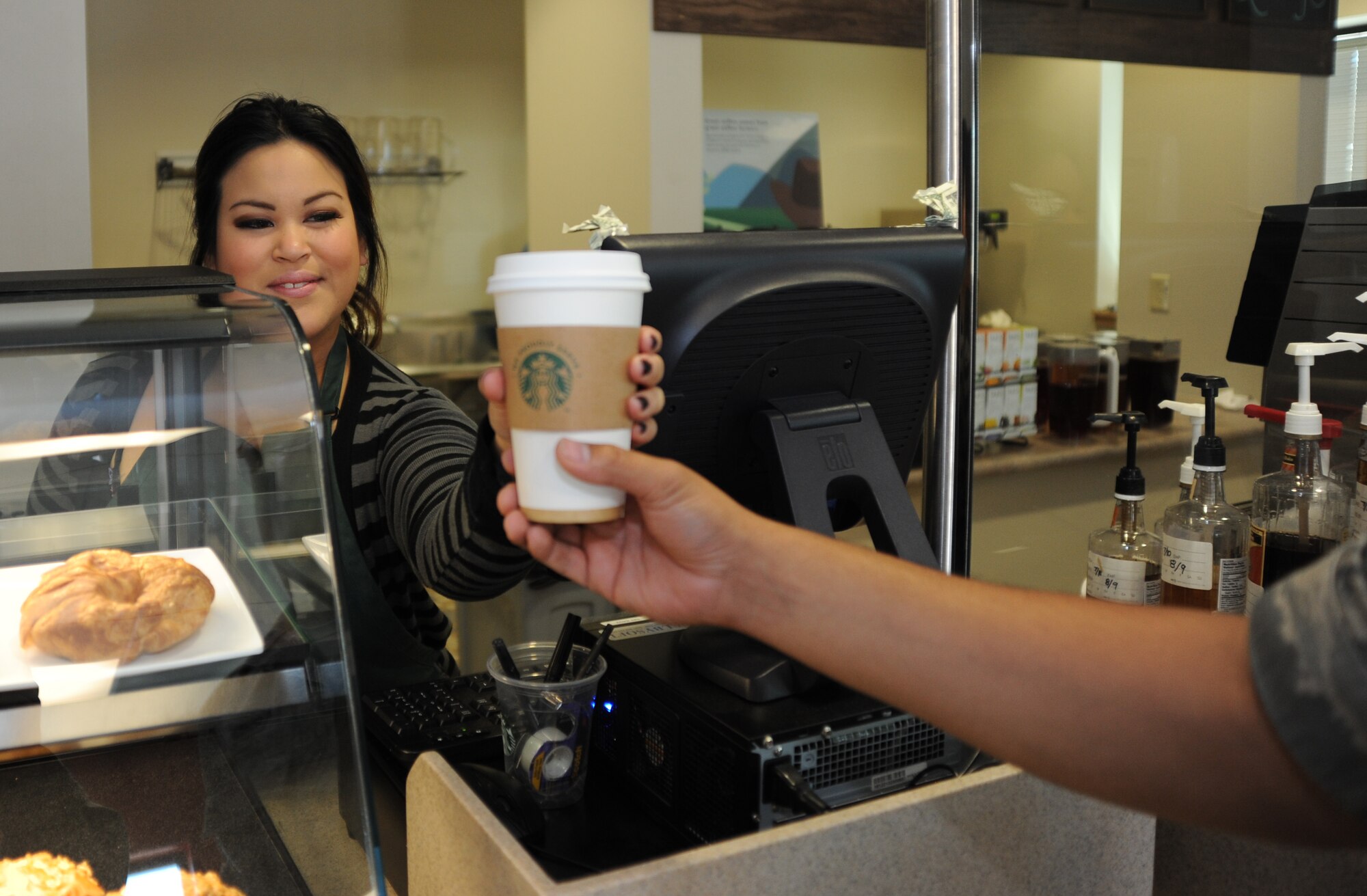 Paula Cayanan, Coolbeans Cafe manager, serves a hot cup of java to an Airman Aug. 7, 2014, at Creech Air Force Base, Nev. The new coffee shop is located in Building 1003 and is open from 7 a.m. to 4 p.m. Monday through Friday to provide Airmen coffee, snacks and a relaxing atmosphere. (U.S. Air Force photo by Tech. Sgt. Shad Eidson/Released)