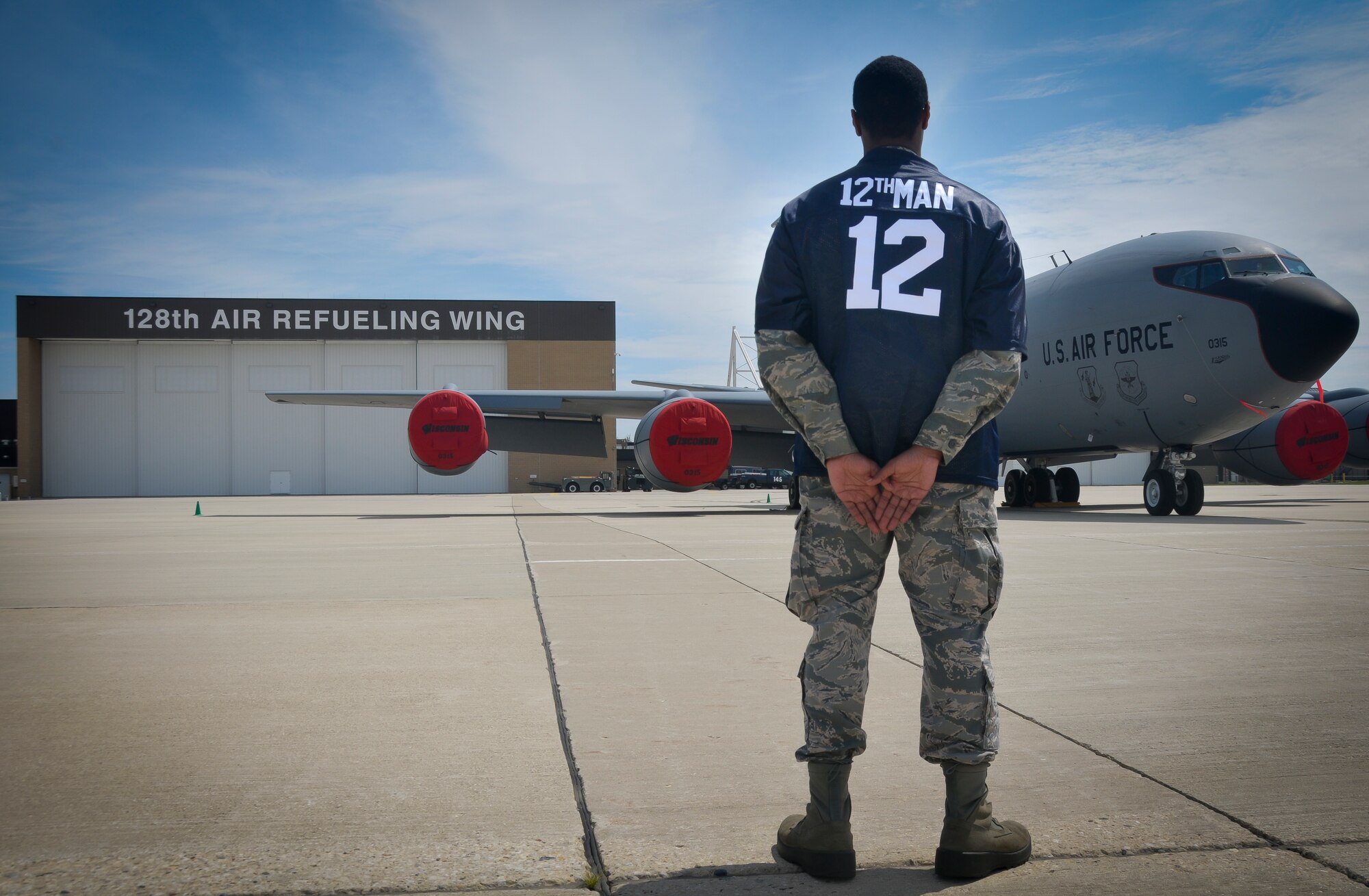 An Airman with the 128th Air Refueling Wing displays the Force Support Squadron 12th Man award jersey in front of a KC-135R Stratotanker here on August 10, 2014. Service members with the 128 ARW FSS created the FSS 12th Man award to recognize those who are reaching above and beyond for their fellow airmen. (U.S. Air National Guard photo by Airman Morgan Lipinski/Released)