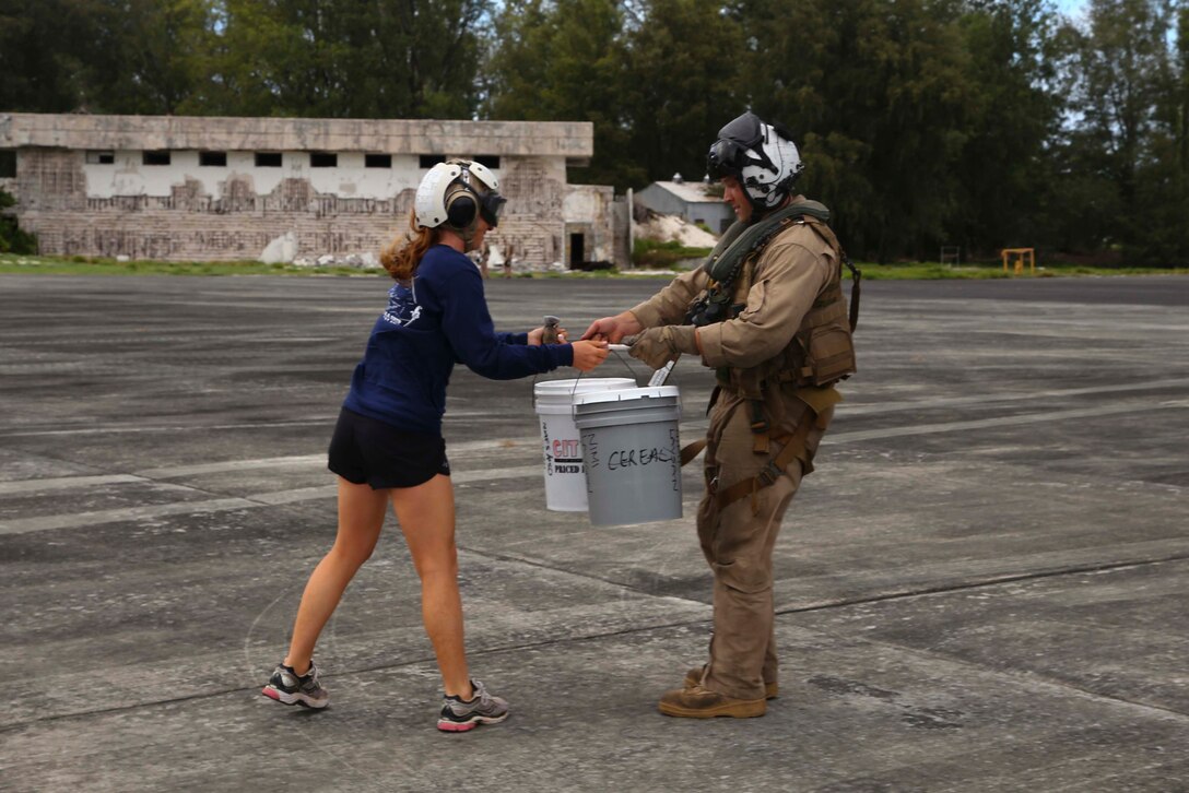 A pilot  with the Marine Medium Tiltrotor Squadron 163 (Reinforced),11th Marine Expeditionary Unit hands over belongings to a  National Oceanic and Atmospheric Administration (NOAA) researcher at Midway Atoll during the MEU’s WESTPAC 14-2 deployment Aug. 8, 2014. Marines and sailors from the 11th MEU and Makin Island Amphibious Ready Group team recovered 11 personnel from three isolated islands more than 900 nautical miles northwest of Hawaii and directly in the path of Hurricane Iselle. MEU aircraft transported the researchers to Midway Atoll where they could seek shelter from the storm. (U.S. Marine Corps photo by Lance Cpl. Laura Y. Raga/Released)