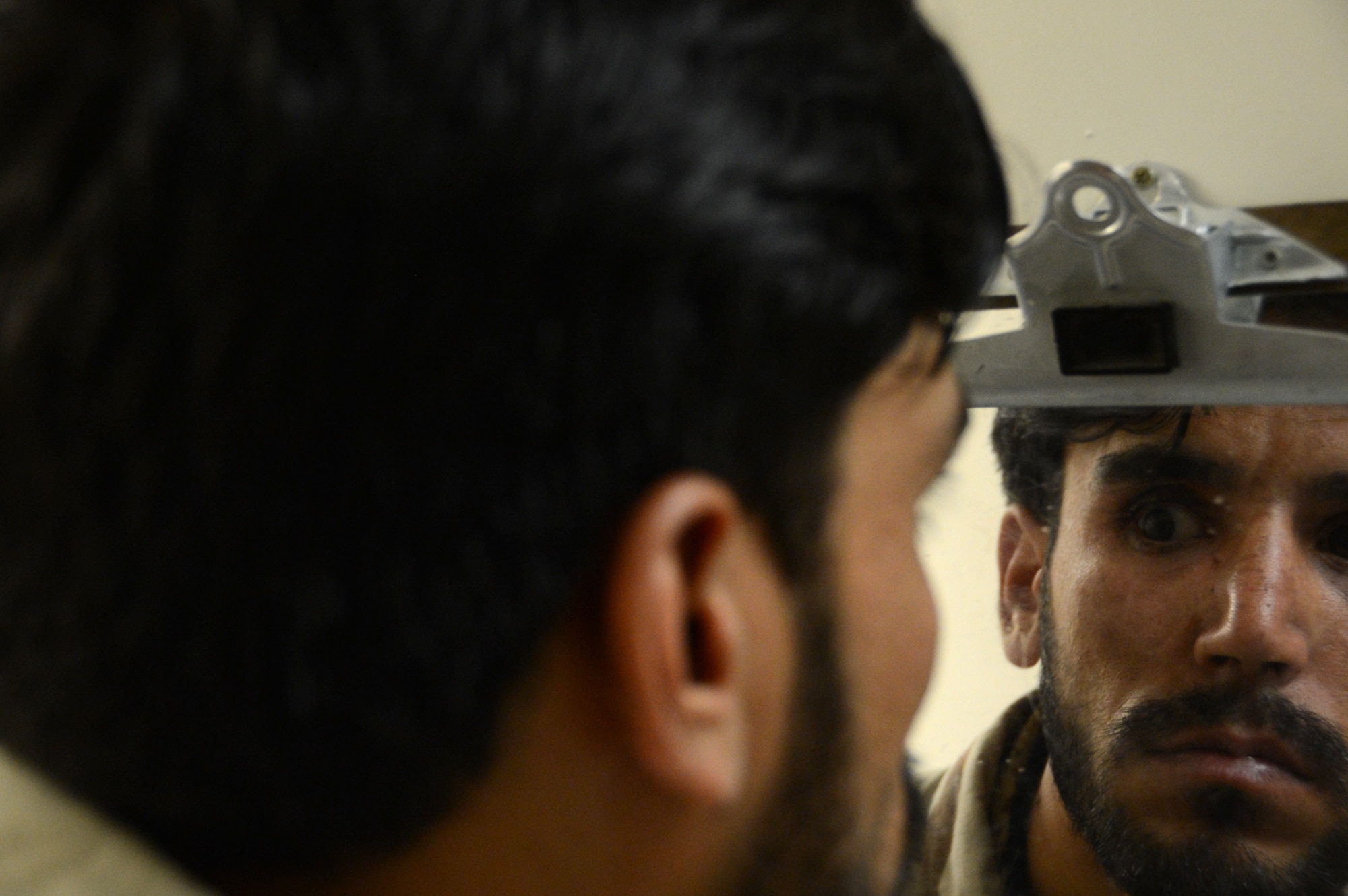 An Afghan soldier looks in the mirror to look at his new prosthetic eye. The soldier had enucleation eye surgery after shrapnel from an explosion hit him in his eye. Enucleation eye surgery is when the eye is removed, but the eye muscles and remaining orbital contents remain intact. (U.S. Air Force photo by Master Sgt. Cohen A. Young/Released)